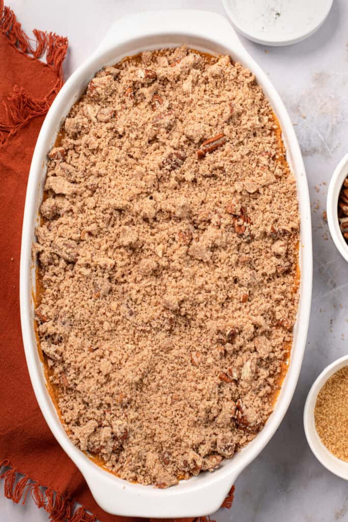 A baking dish filled with unbaked sweet potato casserole and topping.