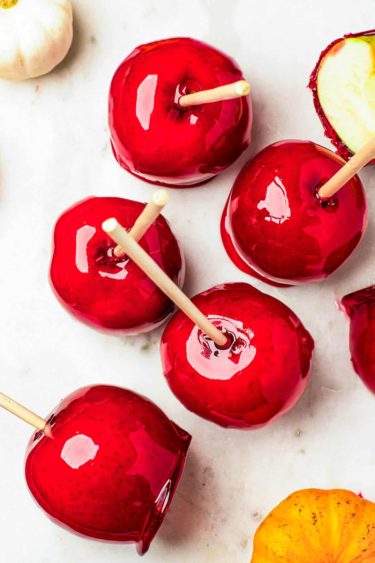 Several candy apples on a white cutting board. Plain Granny Smith apples and an orange fringed placemat in the background.