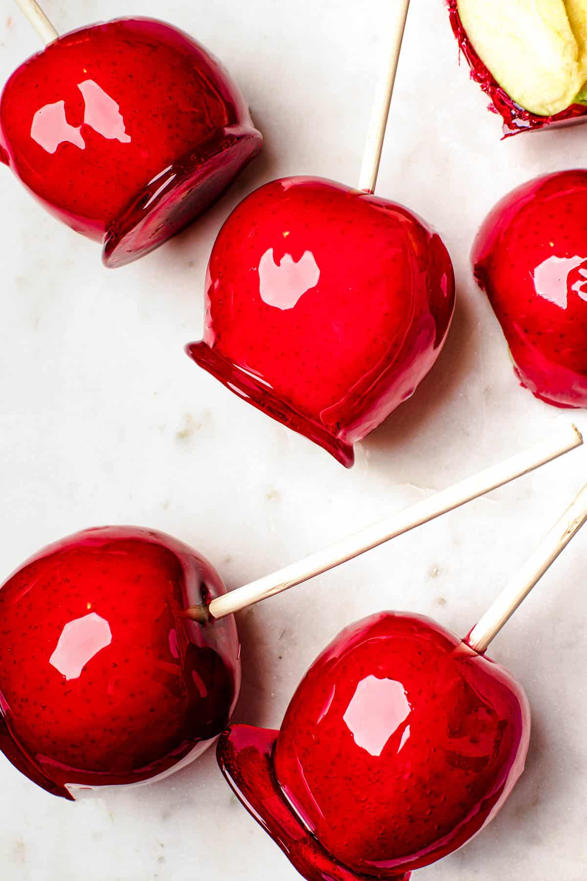 Several candy apples on a white cutting board. Plain Granny Smith apples and an orange fringed placemat in the background.