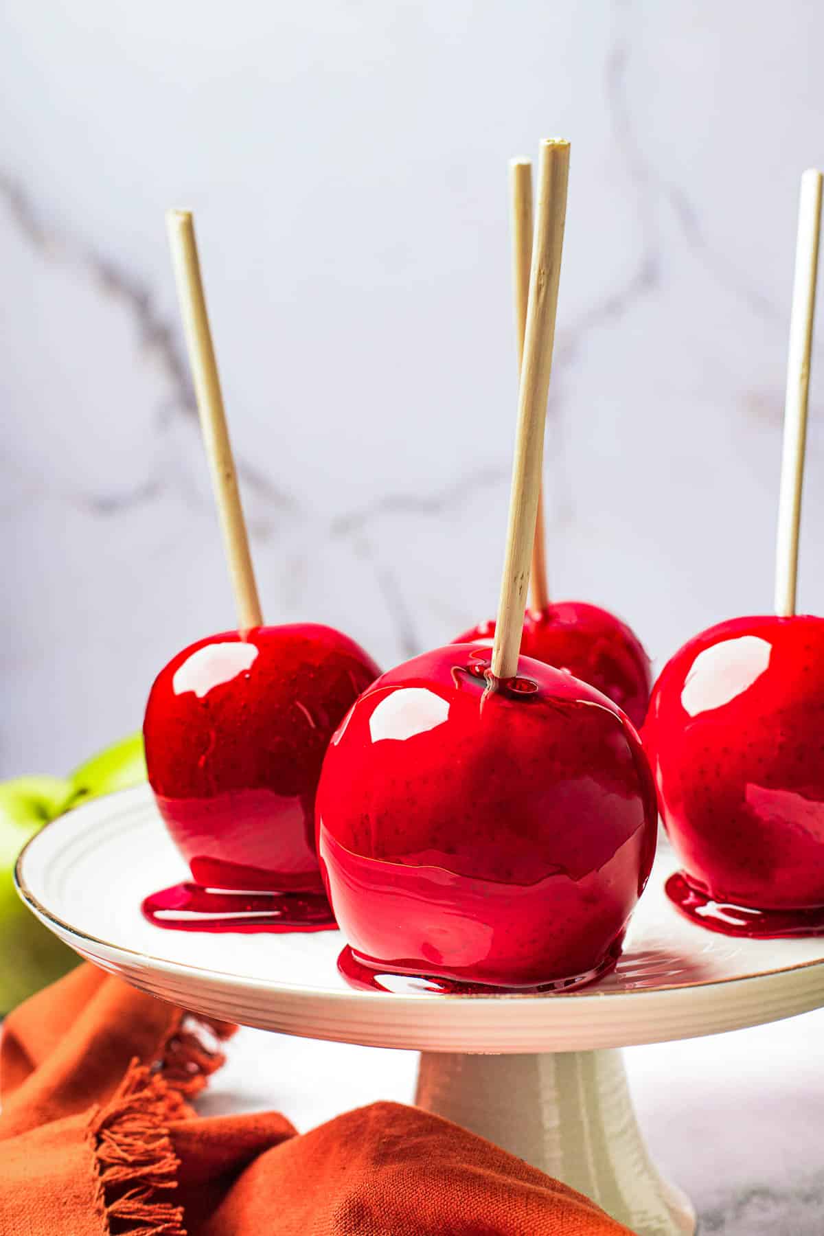A white cake stand with four candied apples displayed on it.