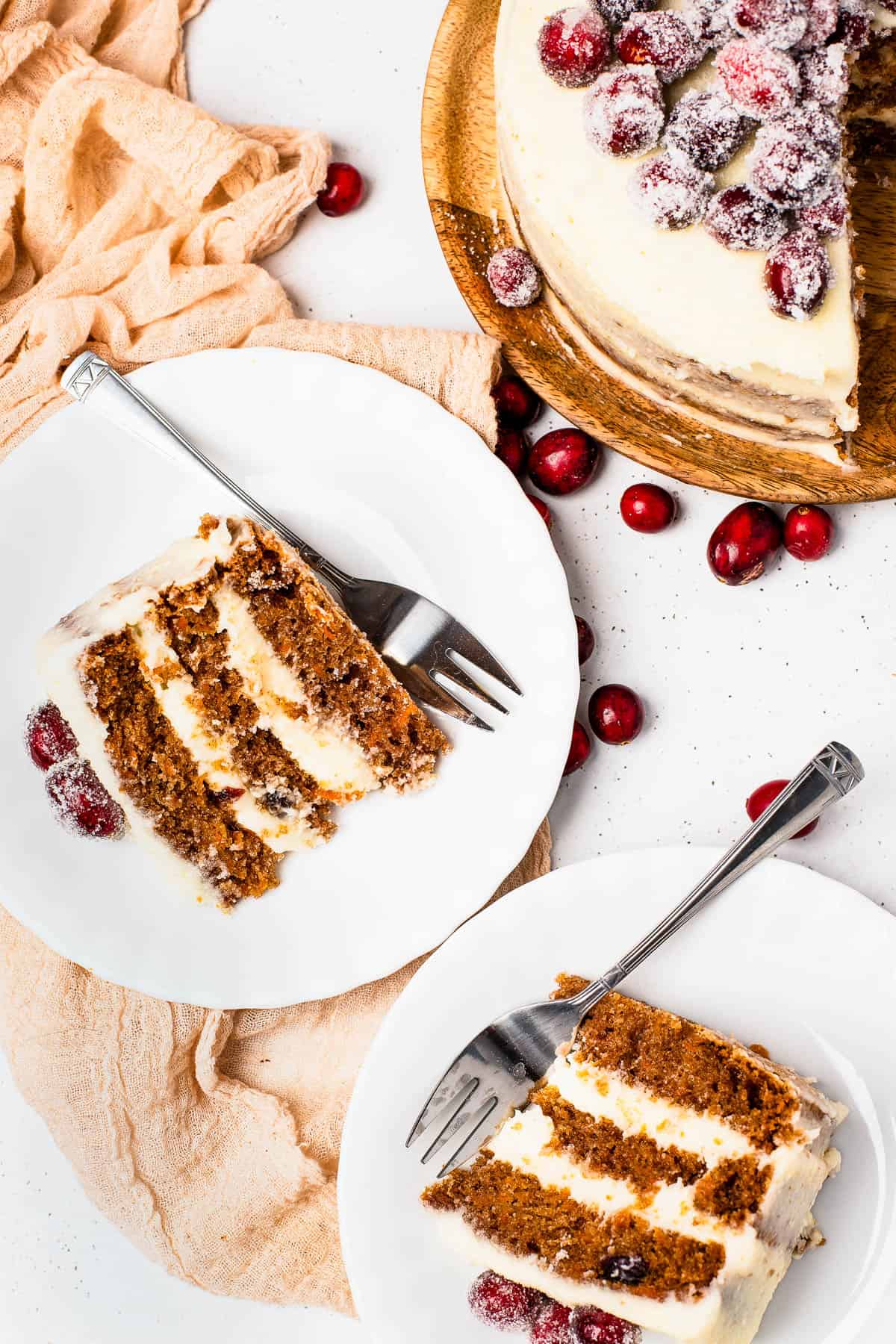 Slices of sugared cranberry layer cake on dessert plates, next to the remaining cake on a cake stand.
