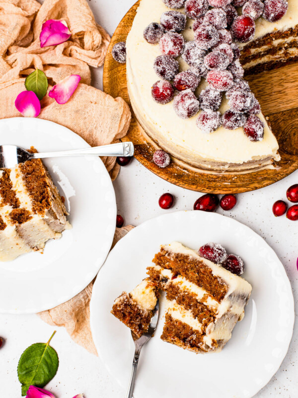 Slices of sugared cranberry layer cake on dessert plates, next to the remaining cake on a cake stand.