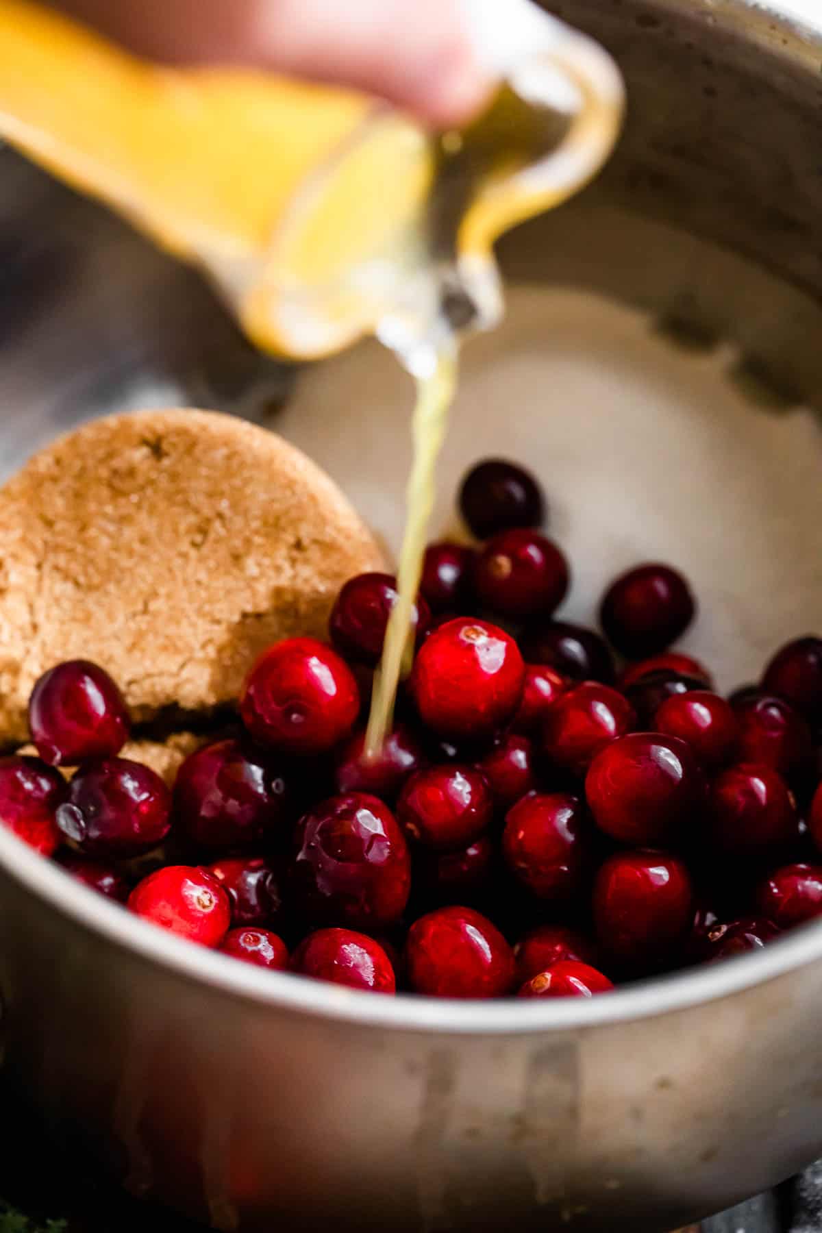 pouring orange juice over fresh cranberries and sugars inside of a saucepan.