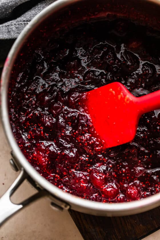 cooking cranberry sauce in a saucepan and stirring through with a red rubber spatula.