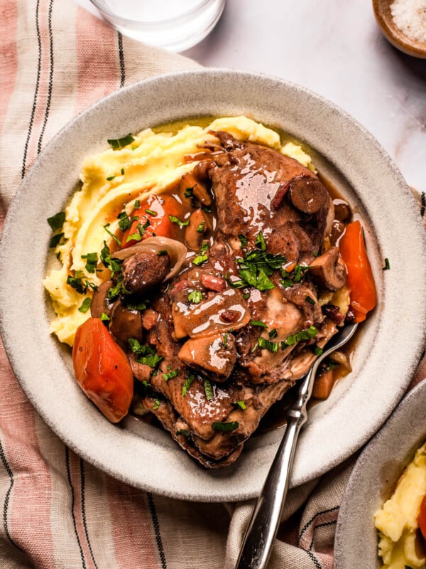 A serving of coq au vin with mashed potatoes on a stoneware plate.