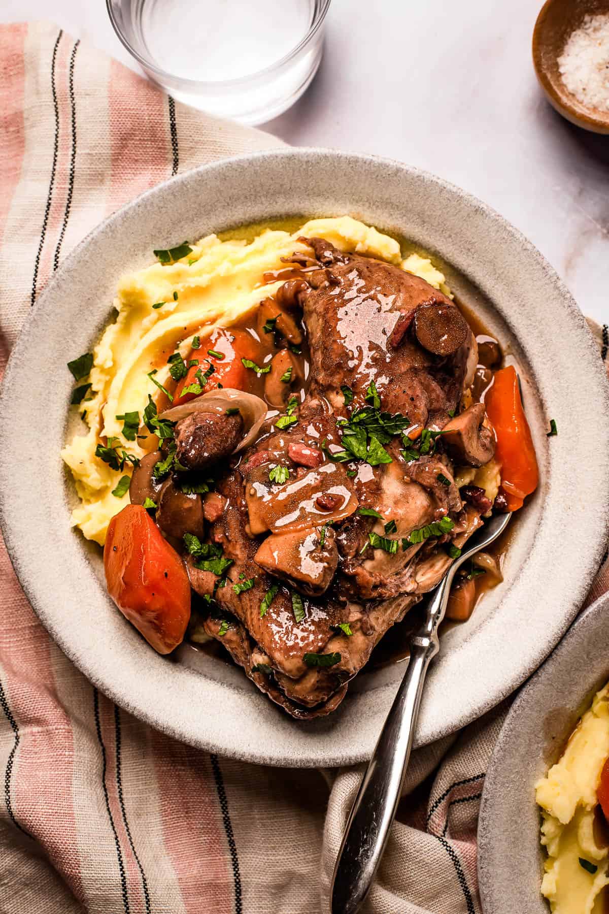 A serving of coq au vin with mashed potatoes on a stoneware plate.