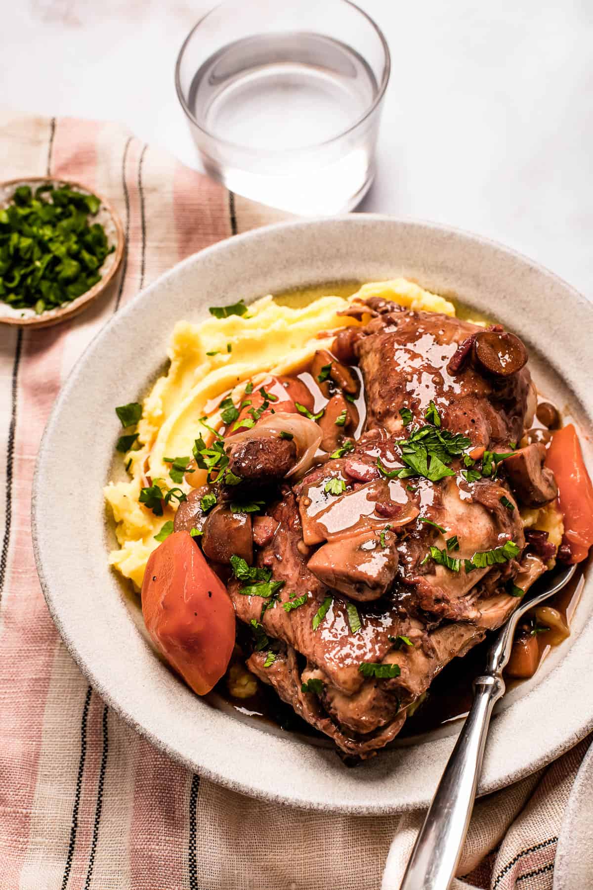A serving of coq au vin with mashed potatoes on a stoneware plate.
