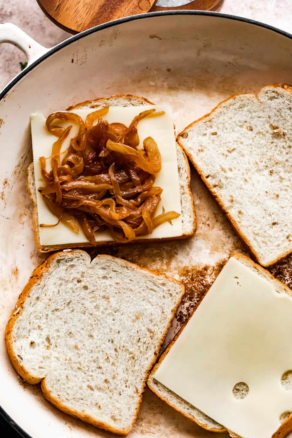 four bread slices in a skillet, with two of the bread slices topped with slices of cheese and one bread slice is topped with caramelized onions.