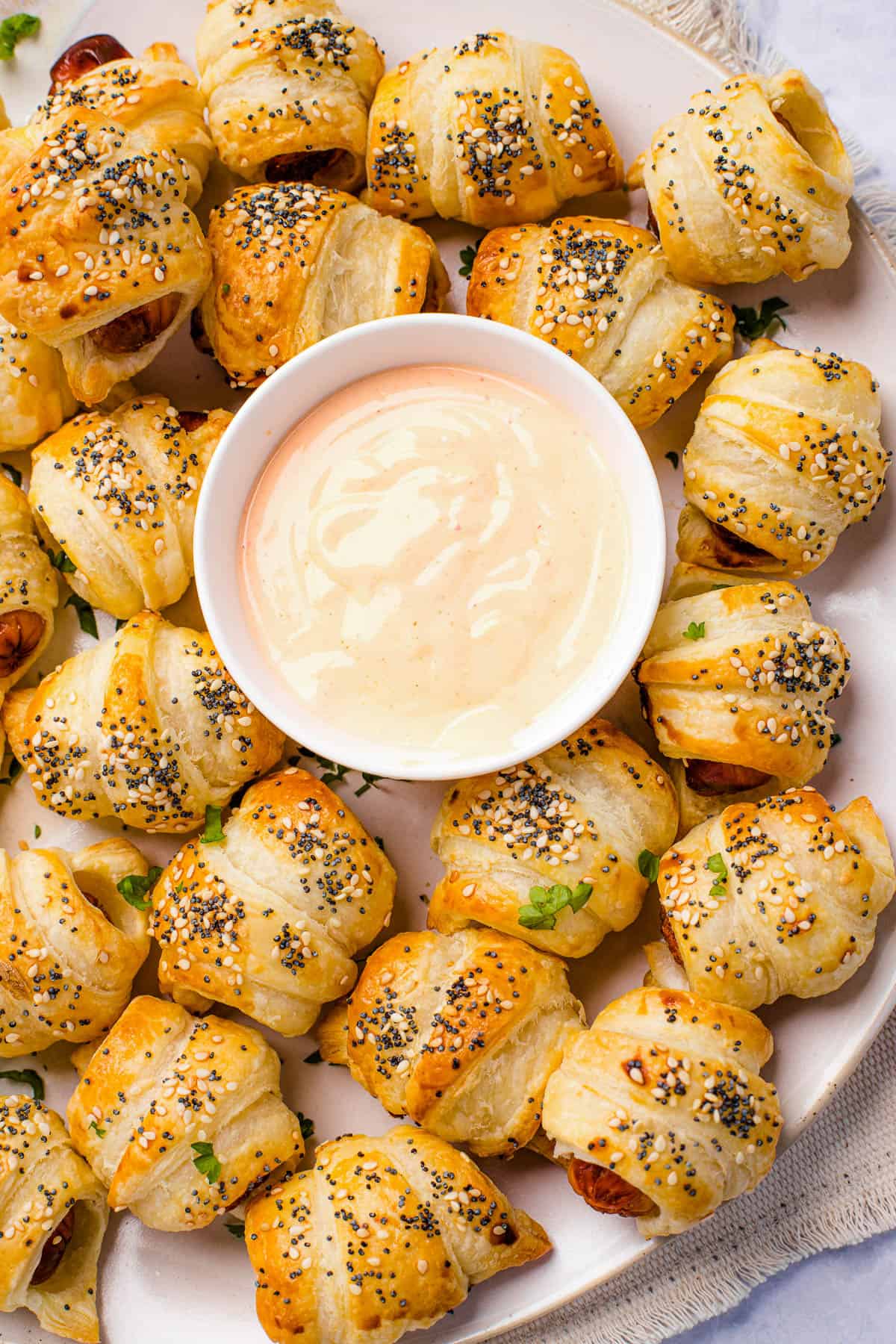 A platter of pigs in a blanket with a bowl of dipping sauce in the center.