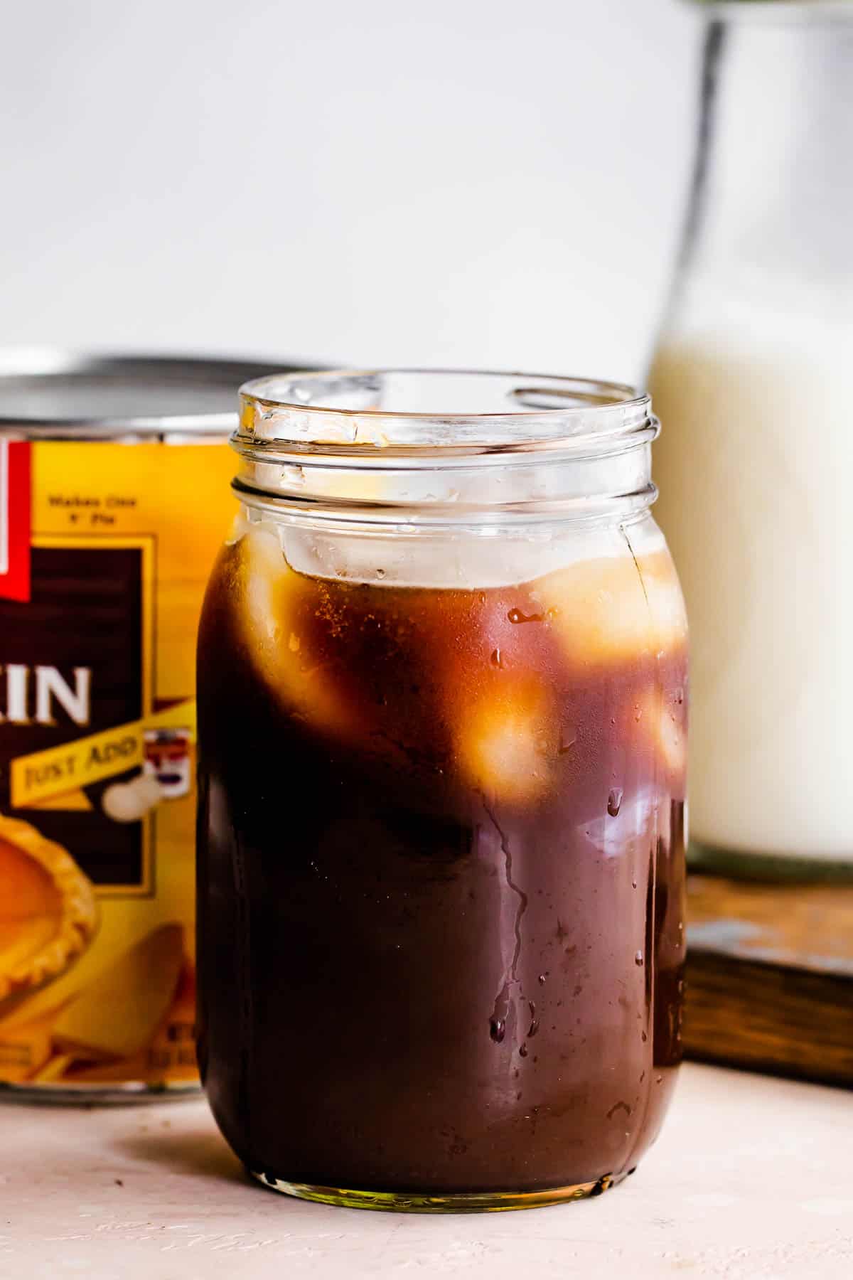 jar filled coffee and ice, with a pumpkin can placed right behind it.