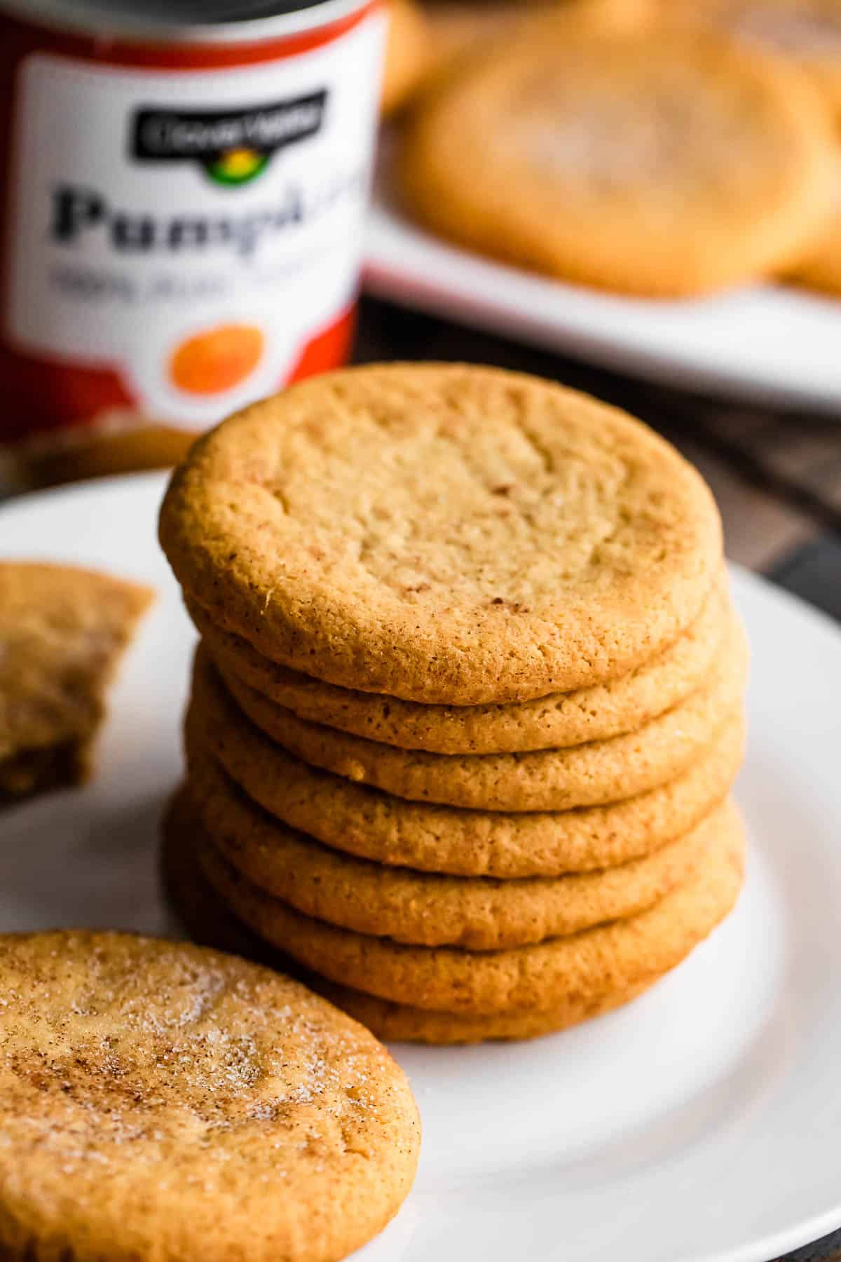 a stack of pumpkin cookies arranged on a white plate with a can of pumpkin set right behind the plate.