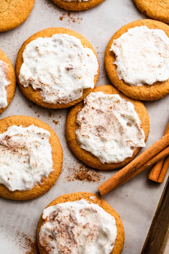 overhead shot of pumpkin cookies topped with cream cheese frosting and arranged on a baking sheet lined with parchment paper.