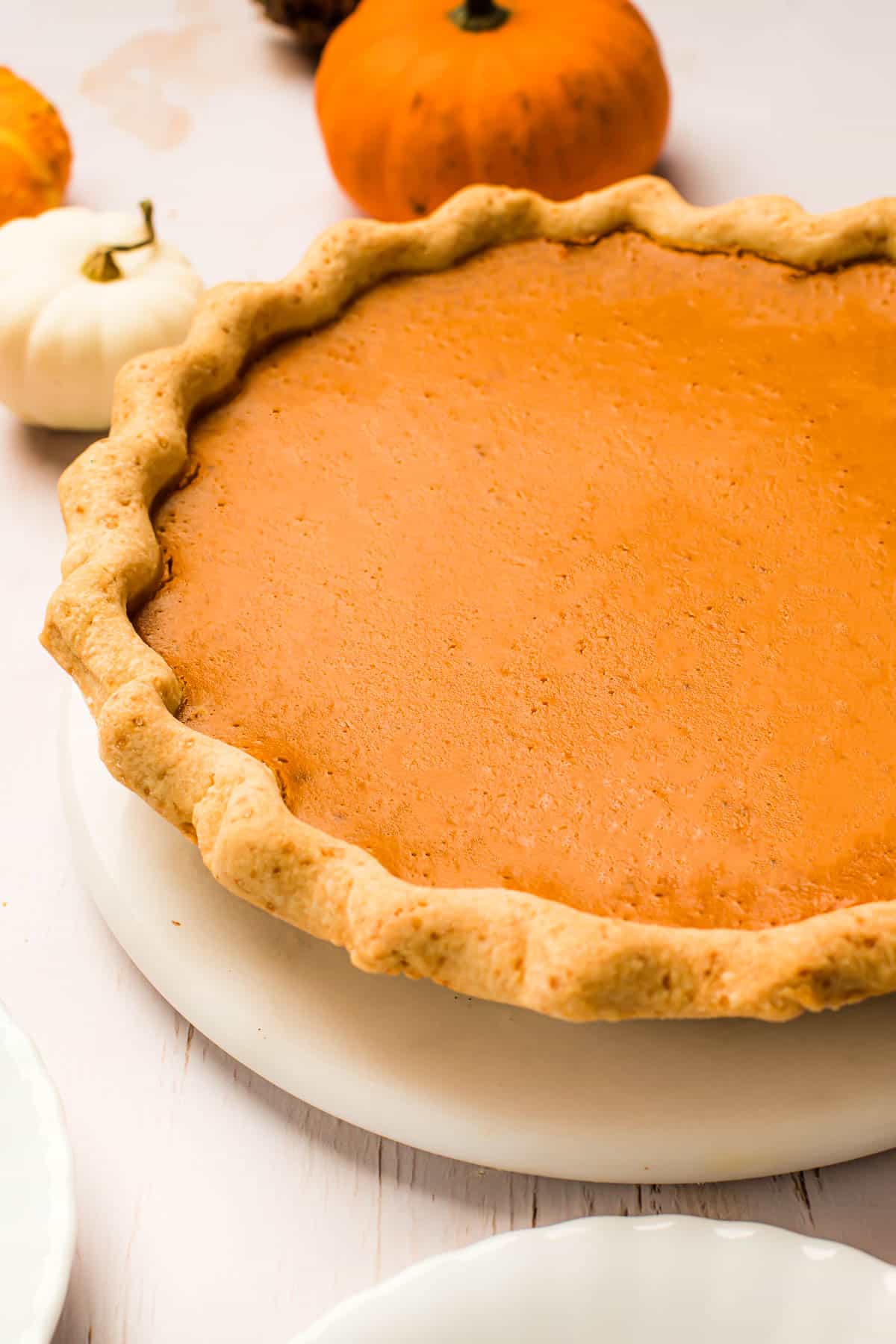 A baked pumpkin pie with a crimped crust on a white serving plate.