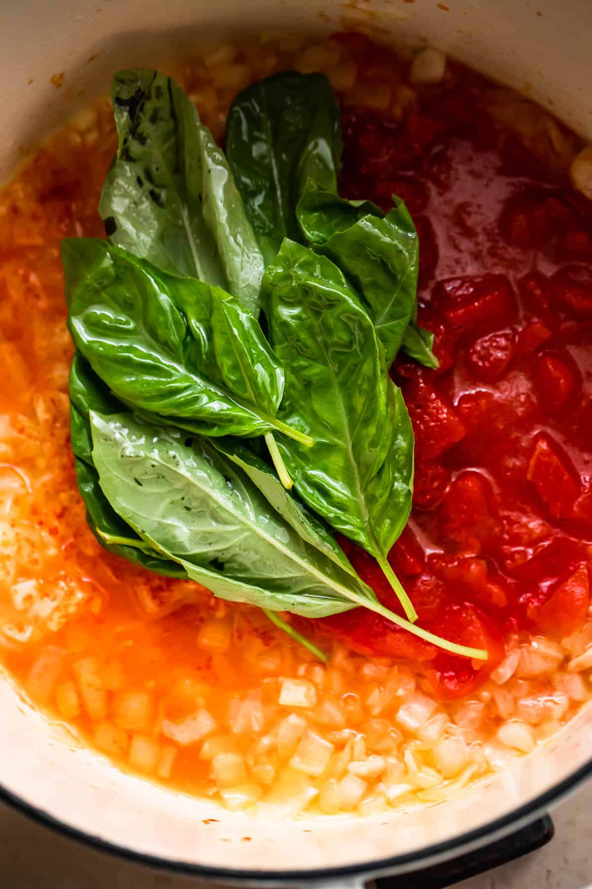 sauteeing canned tomatoes, onions, and basil leaves.