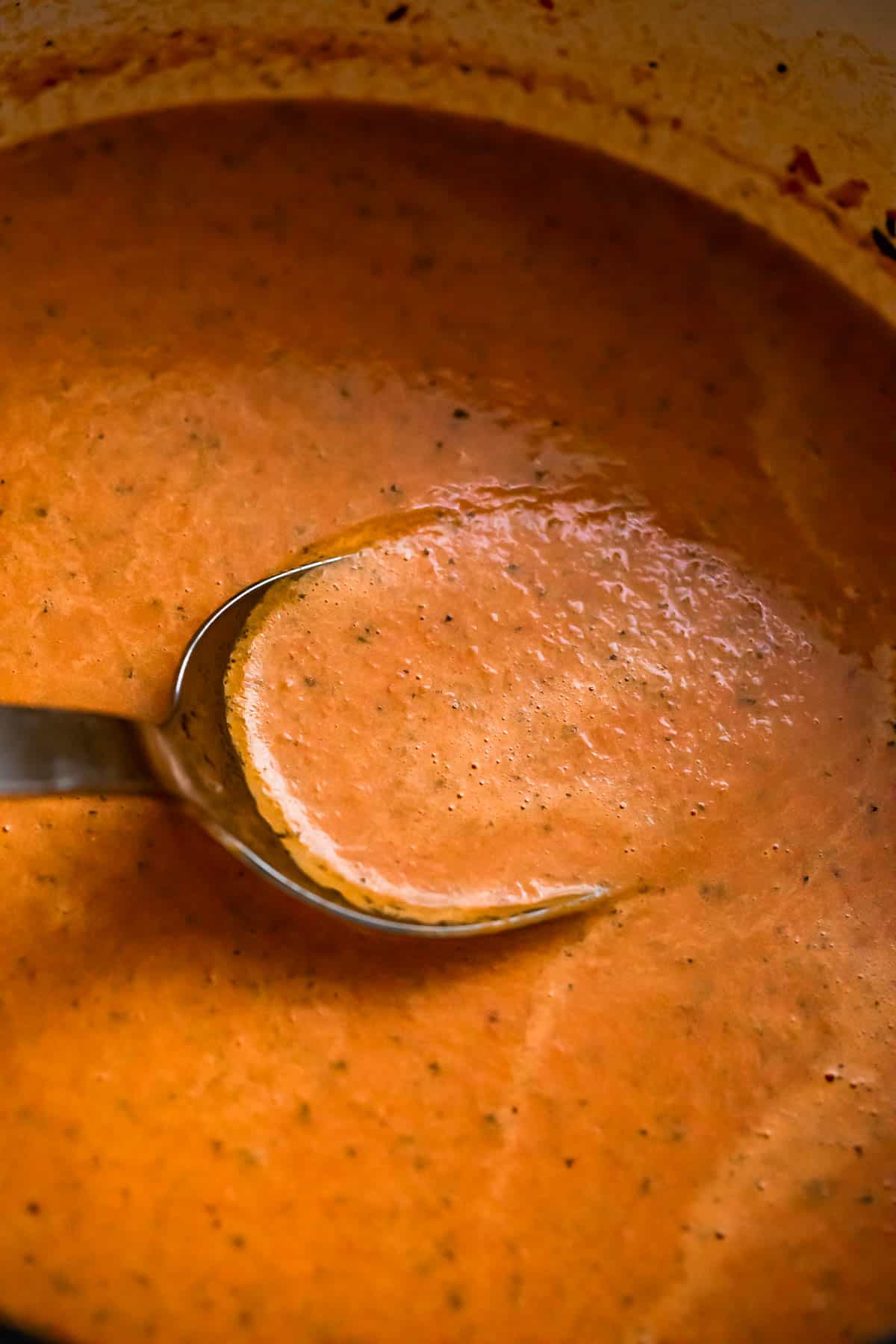 ladle stirring through tomato basil soup inside a soup pot.