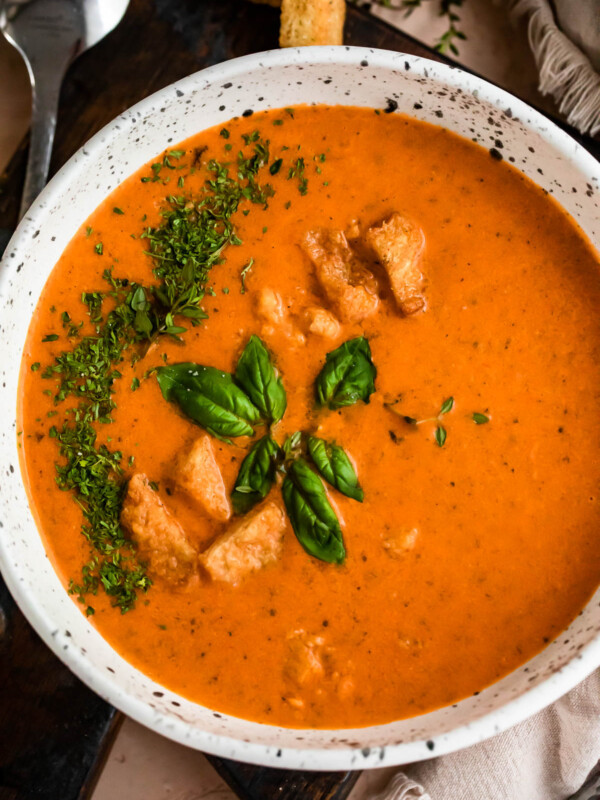 overhead shot of white bowl with tomato basil soup, garnished with croutons, parsley, and basil leaves.