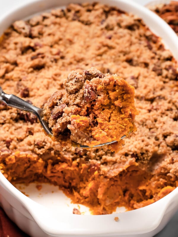 A shot of the sweet potato casserole with a serving spoon lifting a portion out of the dish, showing the texture of the baked casserole mixture and crumb topping.