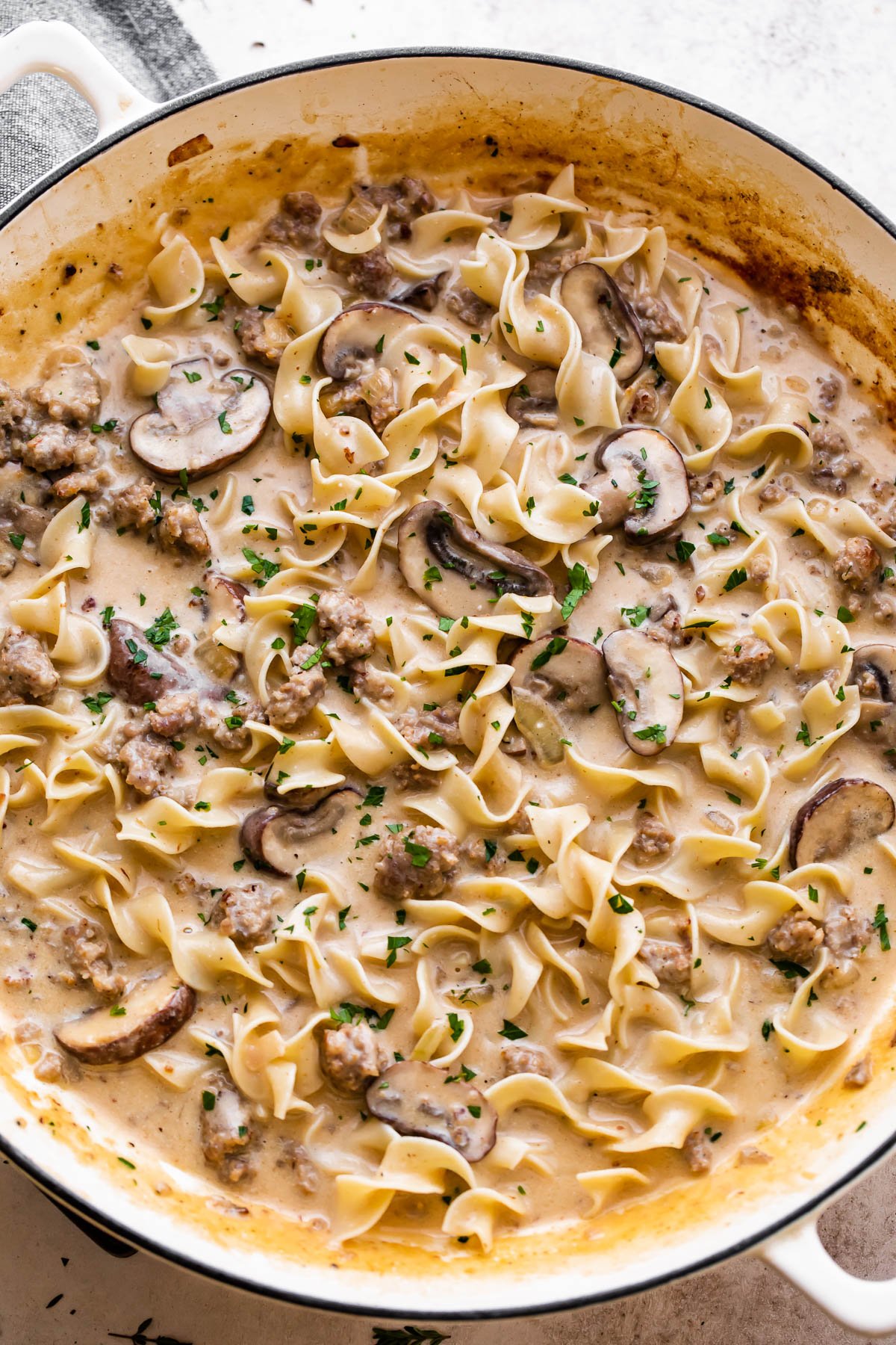 overhead shot of a white braiser filled with cream sauce, noodles, mushrooms, and beef.
