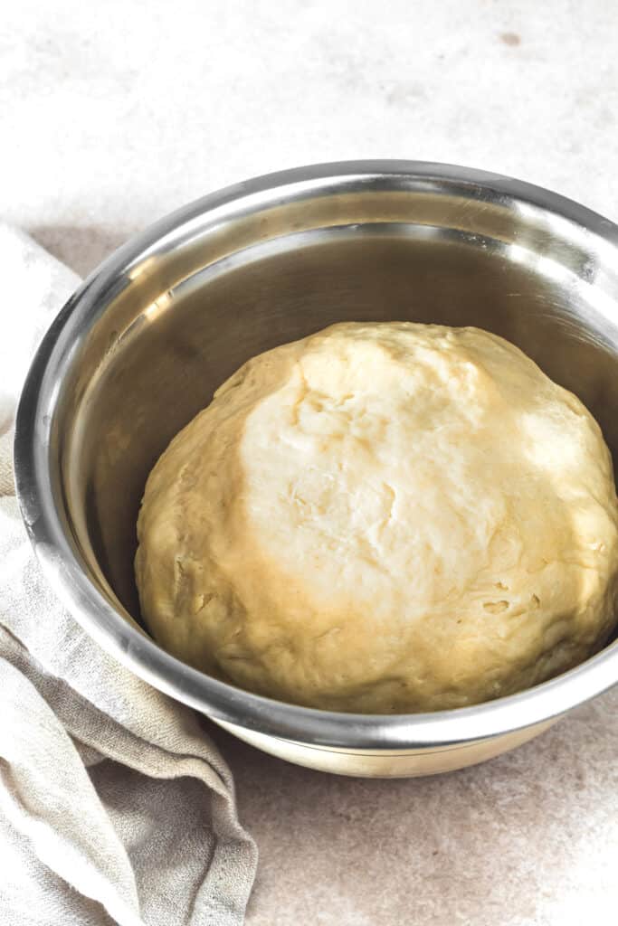 A stainless steel mixing bowl with a ball of soft dough in it.