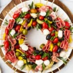 A table with a cutting board holding a wreath of skewers, a small pair of scissors, and fresh rosemary sprigs.