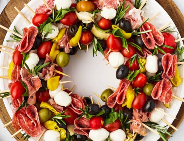 A table with a cutting board holding a wreath of skewers, a small pair of scissors, and fresh rosemary sprigs.