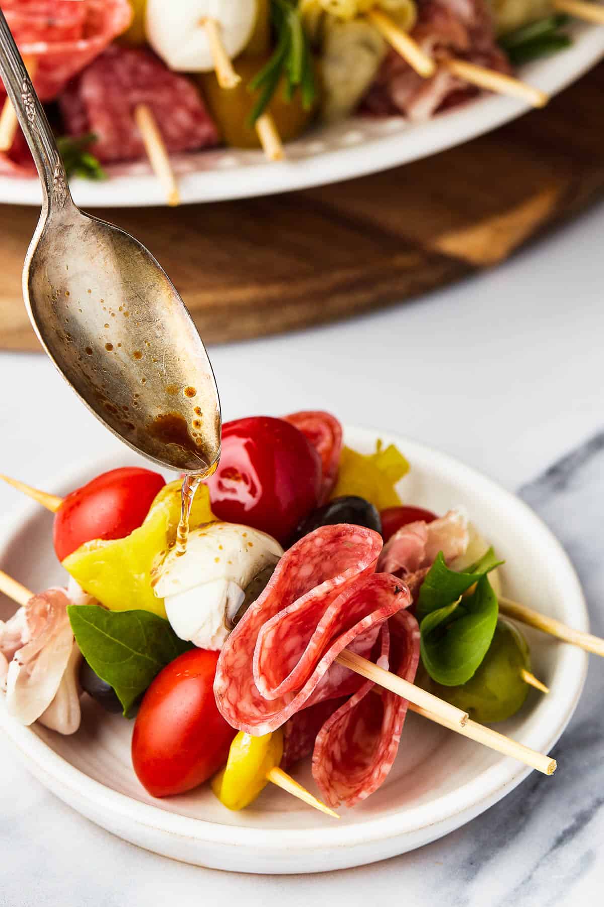 A spoon drizzling balsamic vinegar over a serving of antipasto.