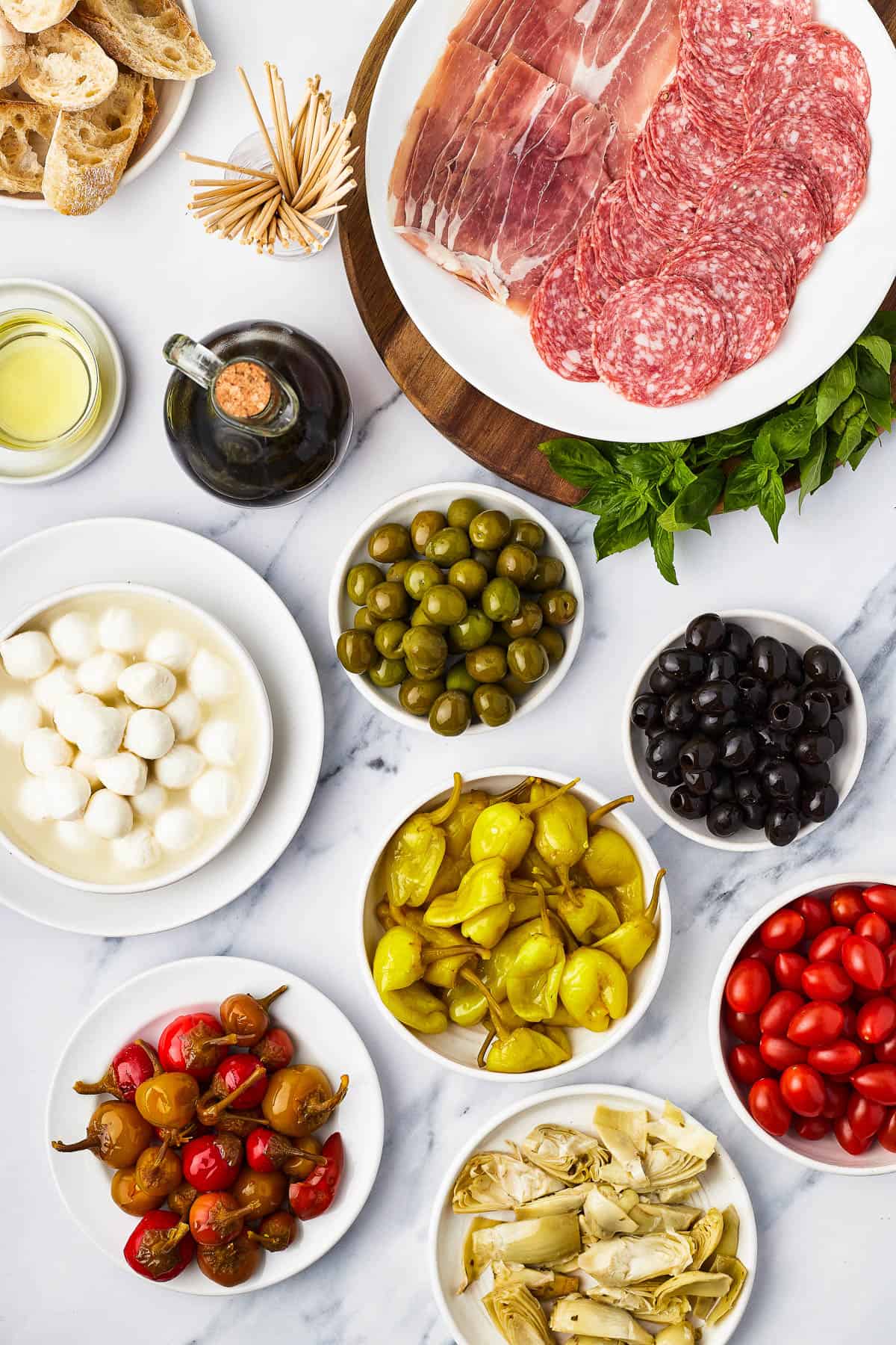 Clockwise from top: Salami and prosciutto slices, green olives, black olives, grape tomatoes, artichoke hearts, pepperoncini, sweet cherry peppers, mozzarella balls, balsamic vinegar, oil, sliced bread.