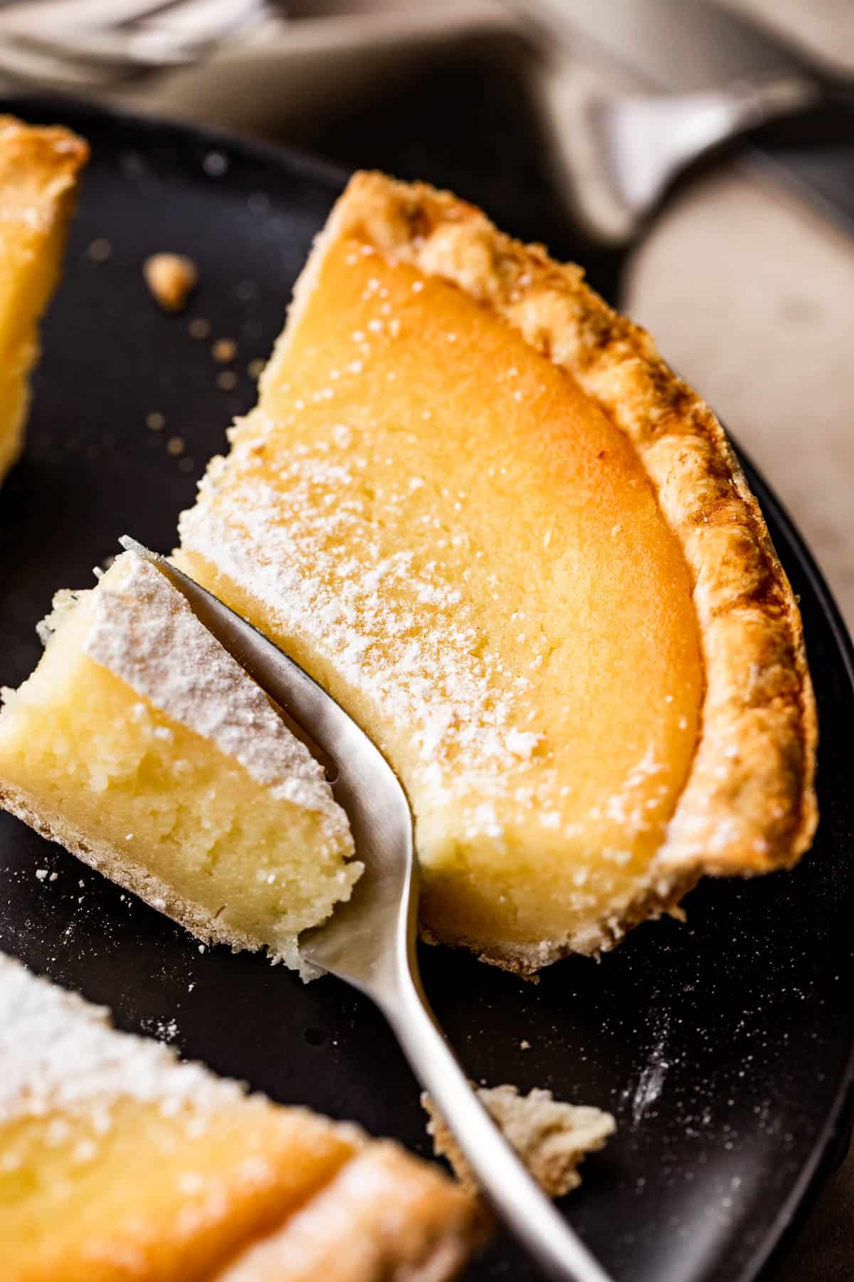 A slice of buttermilk pie on an earthenware saucer with a small dessert fork.