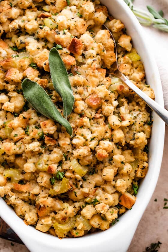 Fresh baked stuffing (dressing) sprinkled with sage leaves and herbs in a white dish.