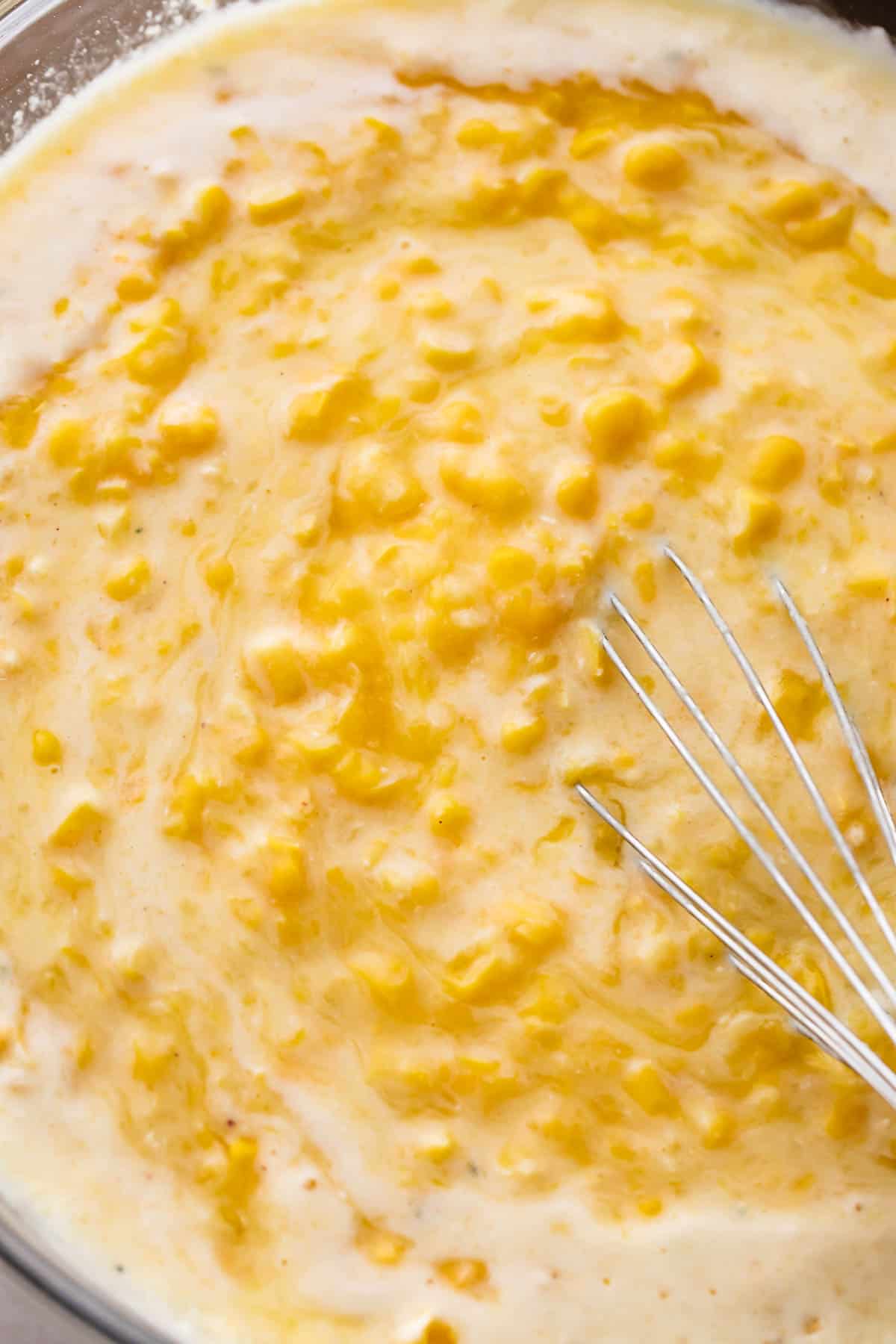 A glass mixing bowl filled with corn pudding batter.