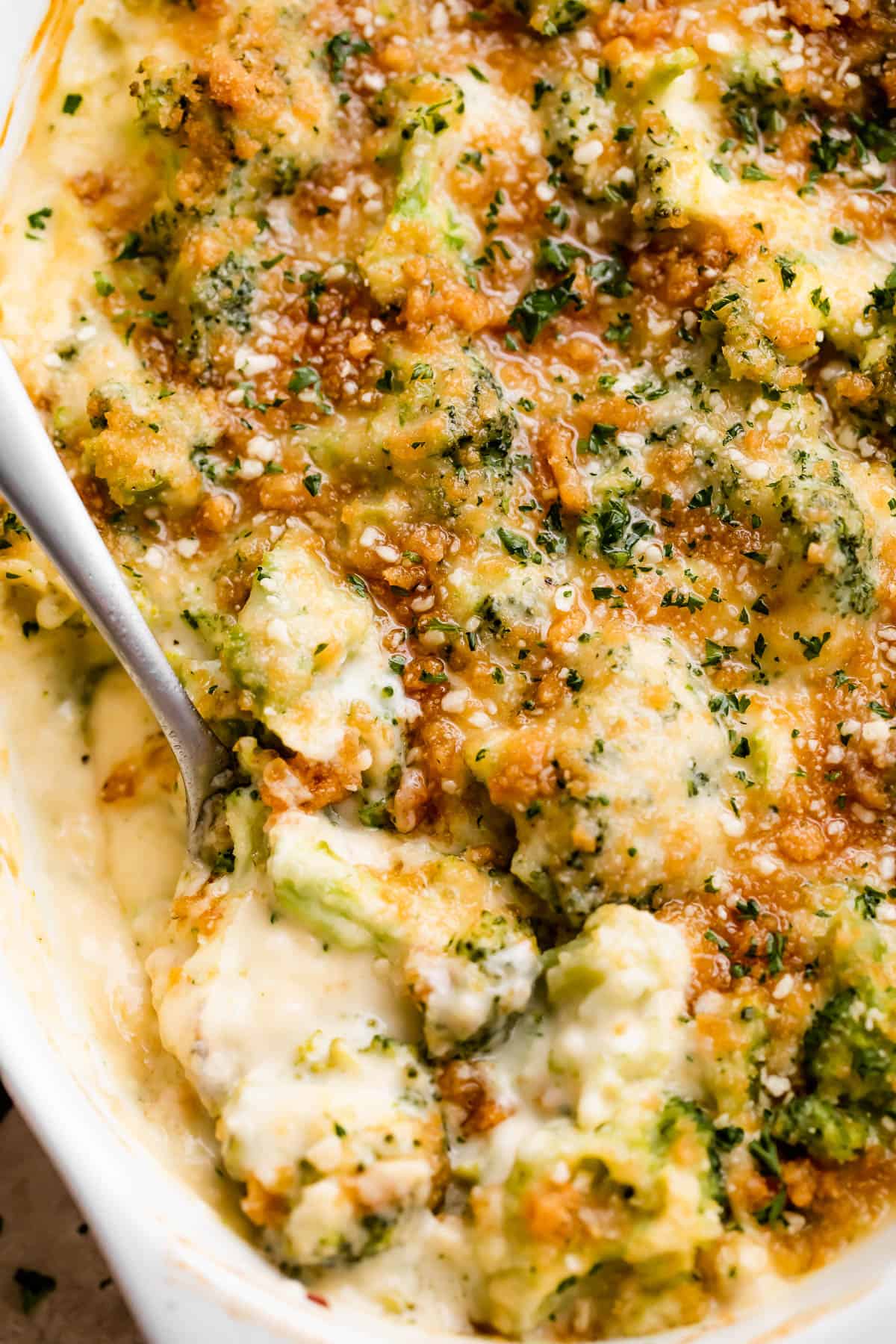 overhead shot of an oval baking dish with Cheesy Broccoli Casserole and a spoon mixing through it.