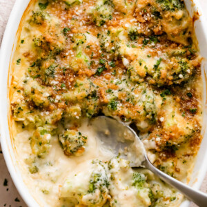 overhead shot of an oval baking dish with Cheesy Broccoli Casserole and a spoon mixing through it.