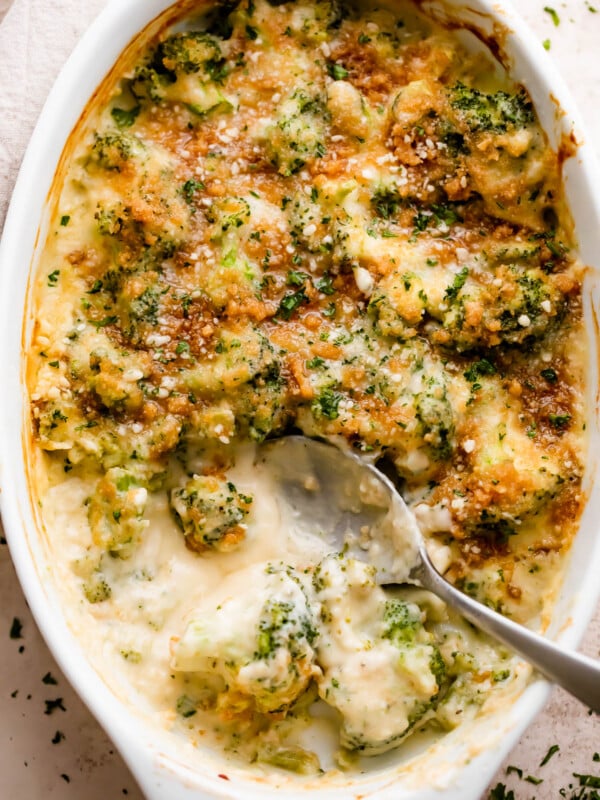 overhead shot of an oval baking dish with Cheesy Broccoli Casserole and a spoon mixing through it.