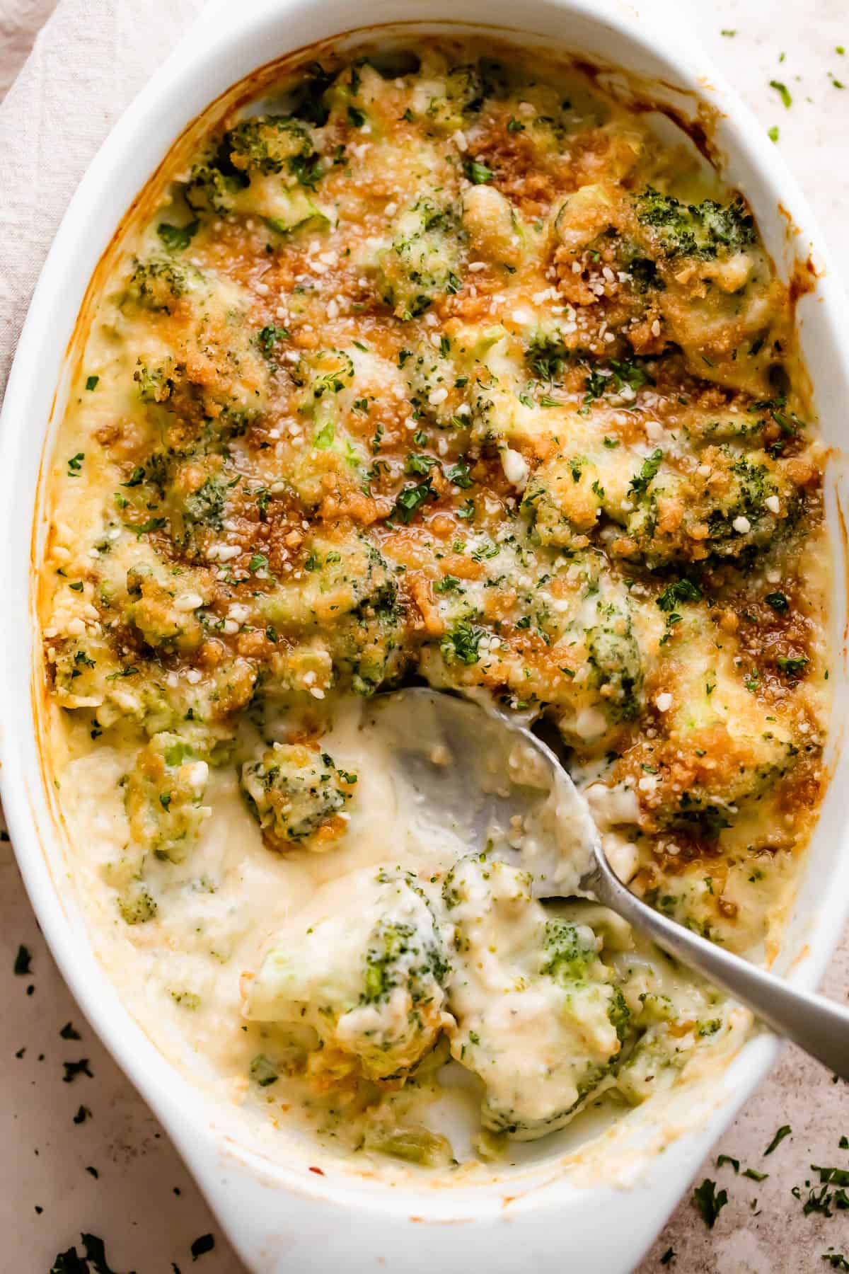 overhead shot of an oval baking dish with Cheesy Broccoli Casserole and a spoon mixing through it.