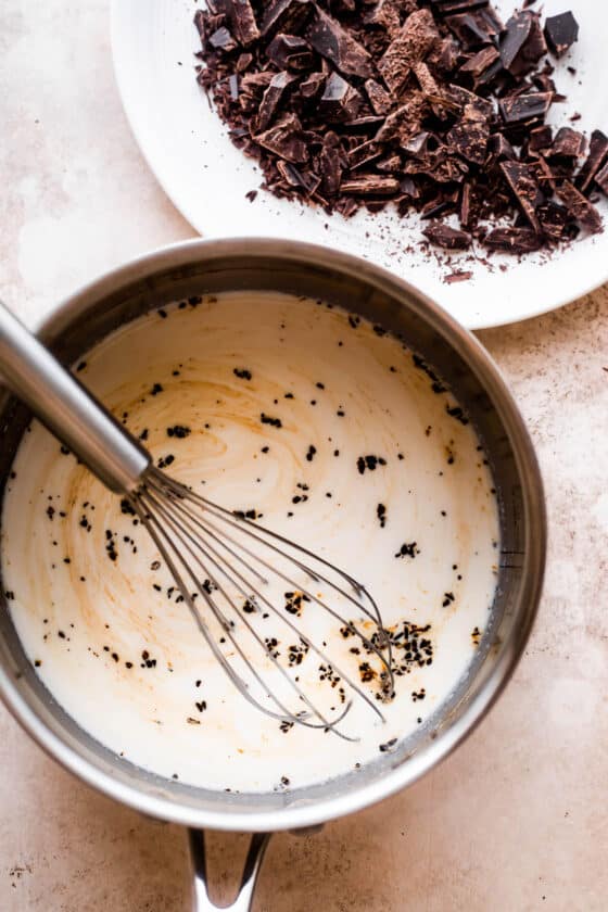 overhead shot of a saucepan filled with heavy cream and a plate with chopped chocolate placed nearby.