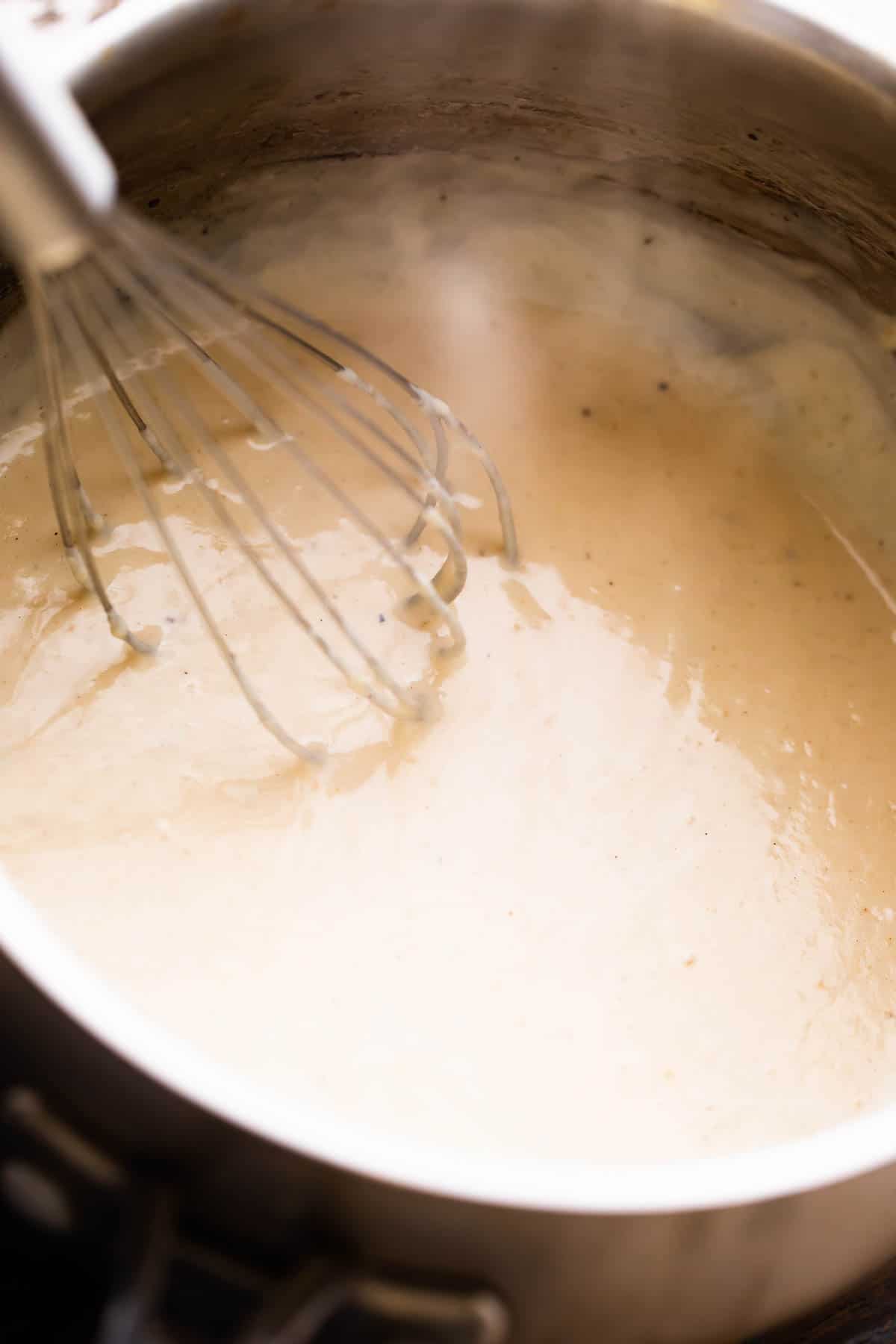 making cream of chicken from scratch in a saucepan and a whisk mixing through it.