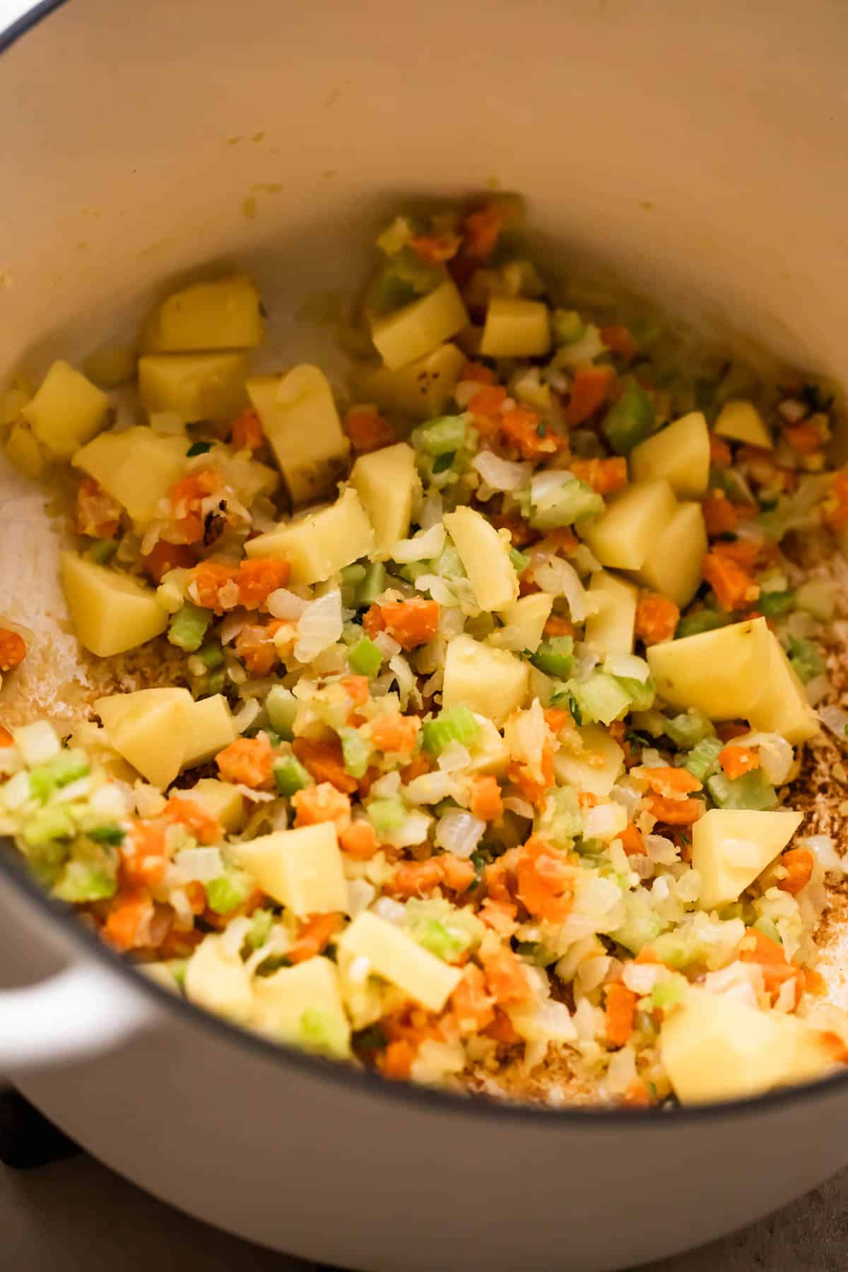 sauteeing carrots, celery, and cubed potatoes in a white dutch oven.