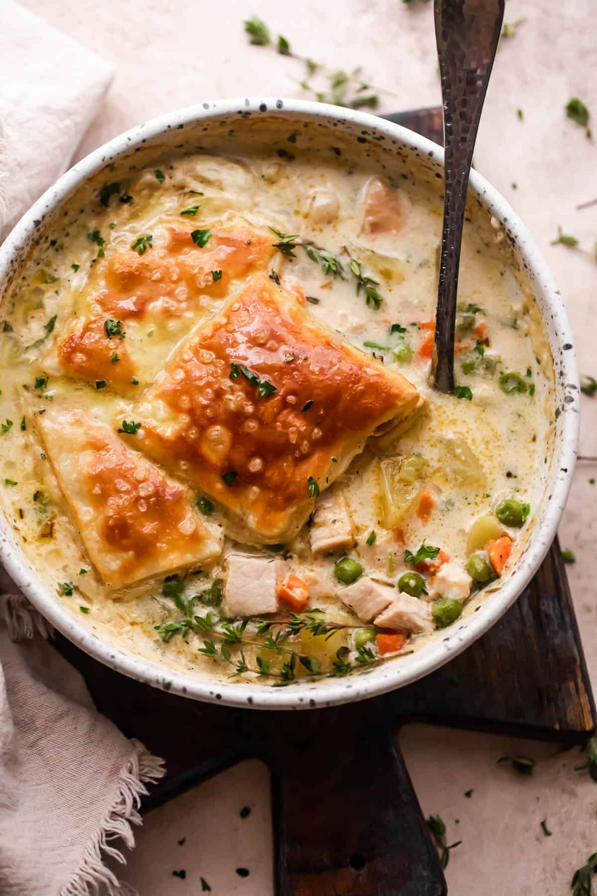 overhead shot of a cream colored bowl filled with turkey pot pie soup and topped with a piece of puff pastry square.