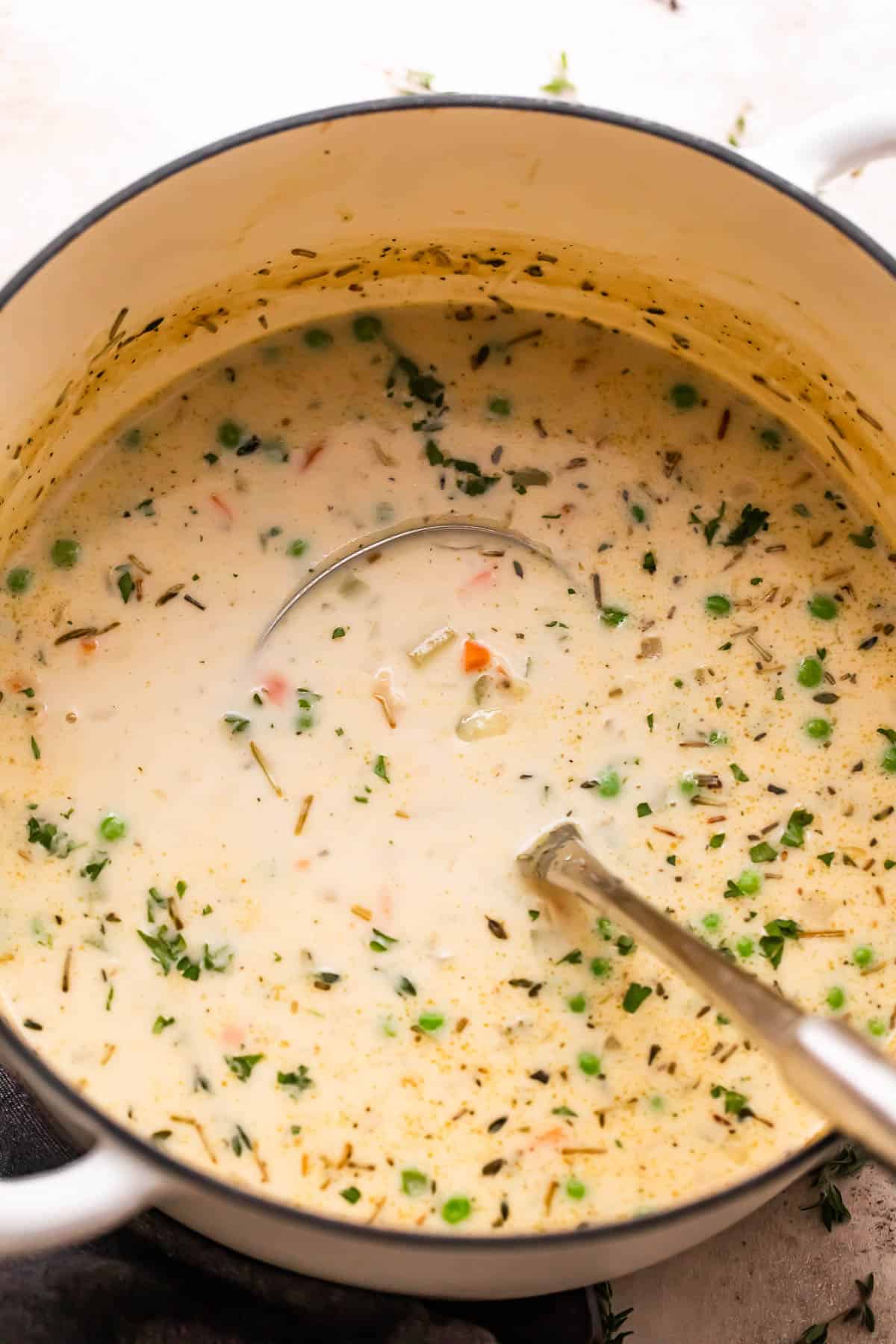 overhead shot of turkey pot pie soup in a white dutch oven with a ladle inside the pot.