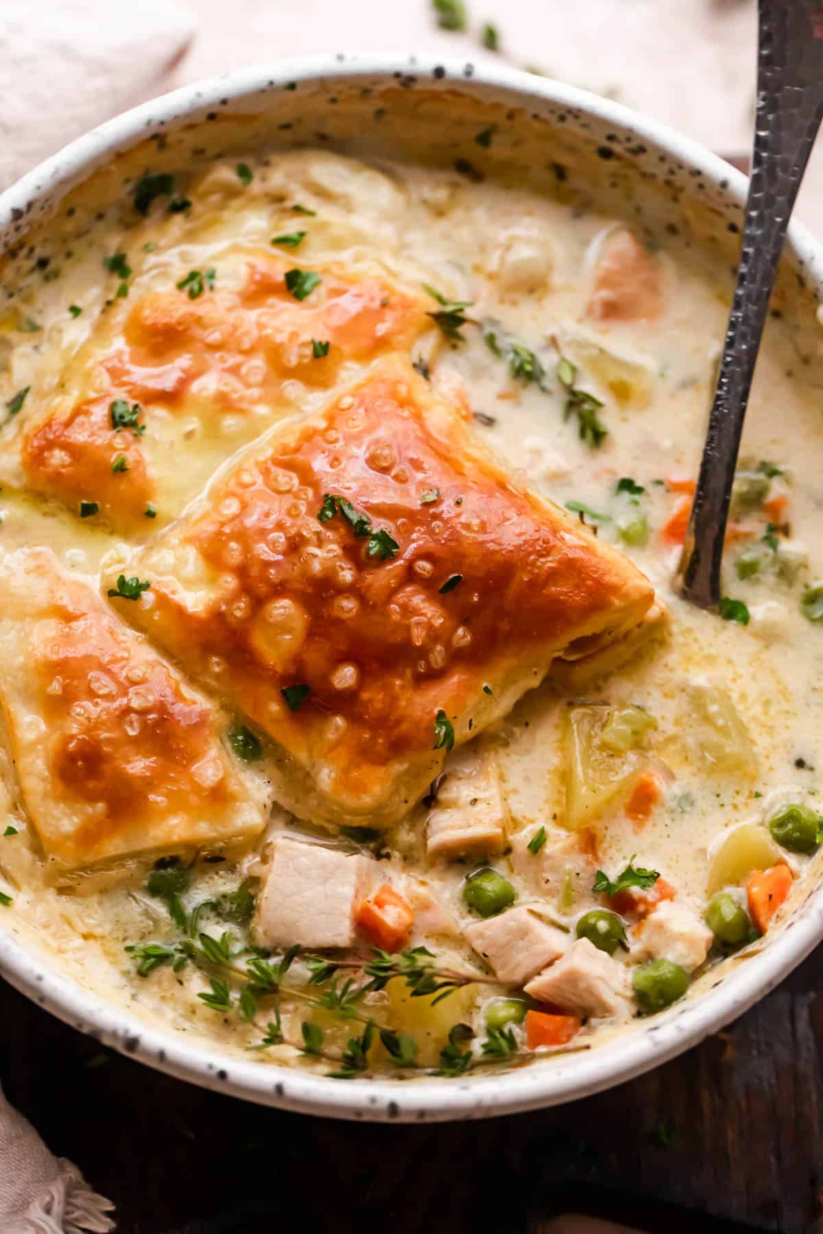 overhead shot of a cream colored bowl filled with turkey pot pie soup and topped with a piece of puff pastry square.