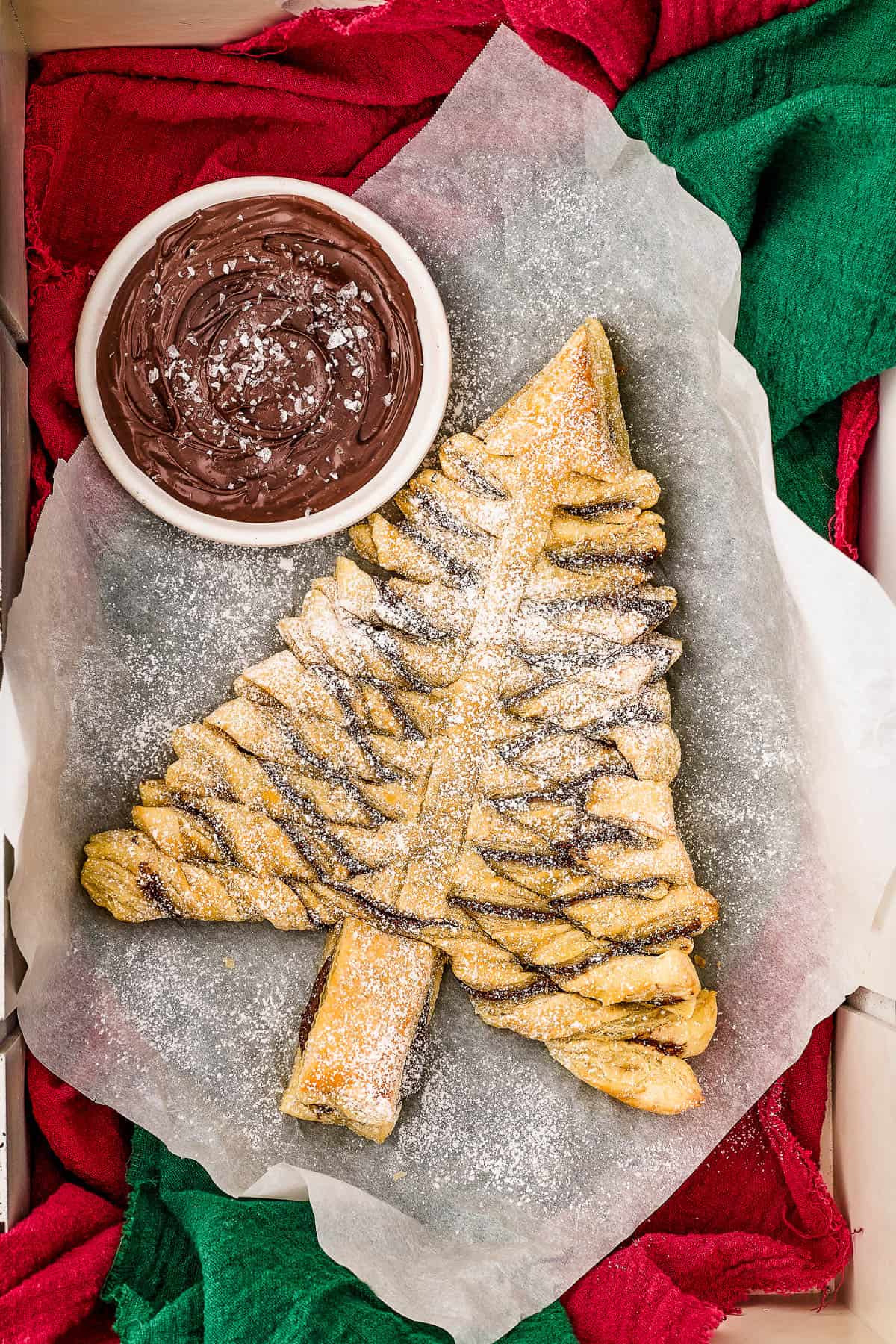 A baked Nutella tree on a piece of parchment, laid over green and red napkins. A bowl of salted Nutella dip sits nearby.