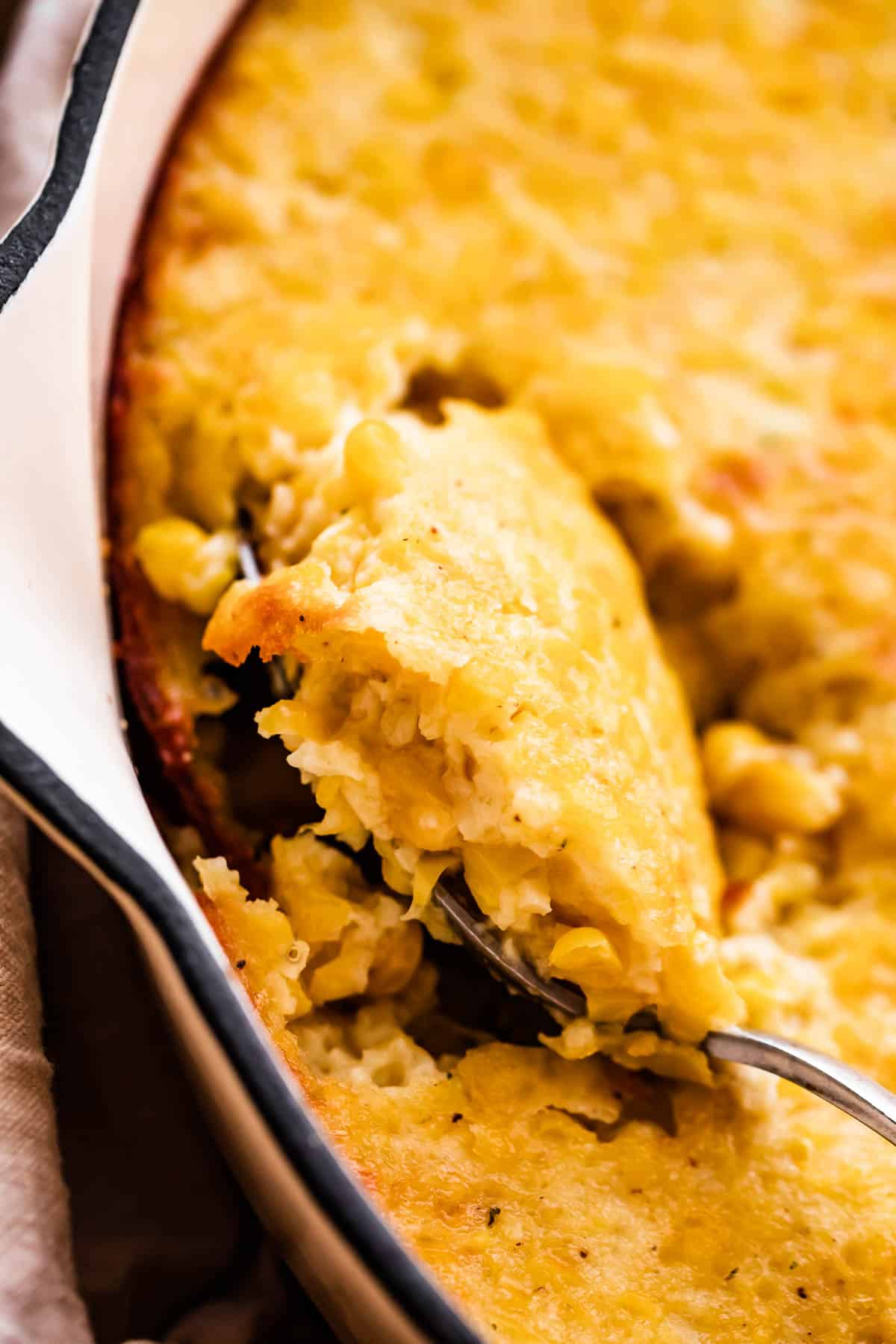 Close-up shot of baked corn casserole in a white skillet with a spoon.