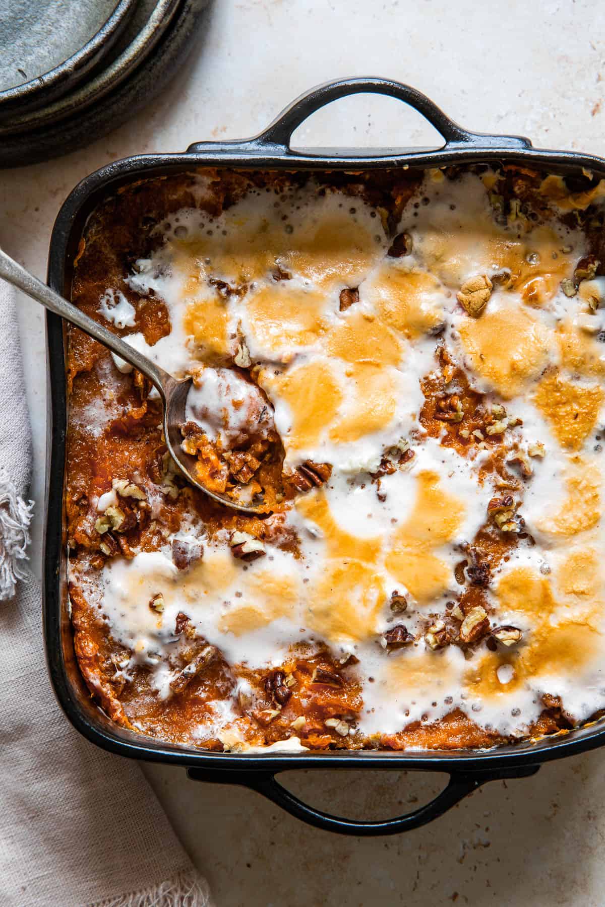 A serving spoon resting in a square black baking dish of sweet potato casserole.