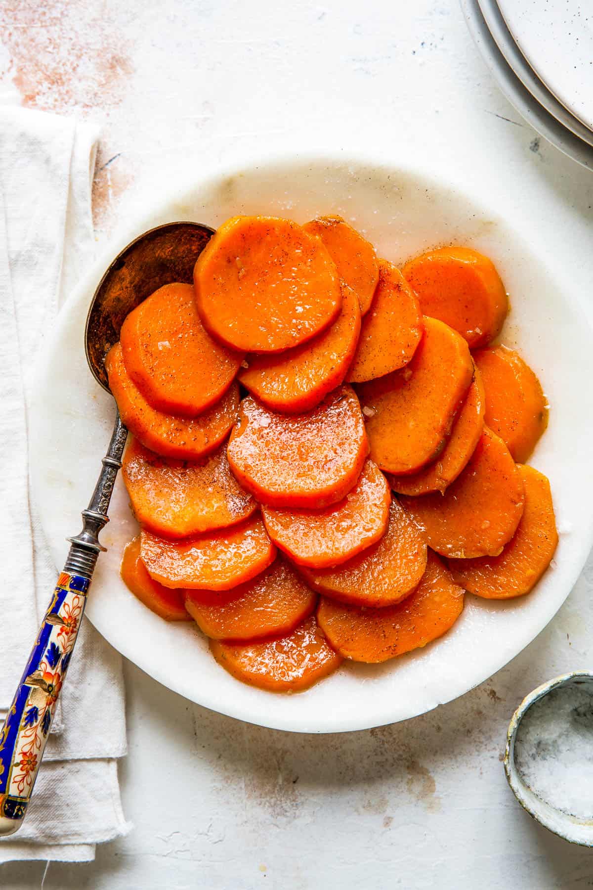 A white serving dish with sliced candied sweet potatoes and a serving spoon.