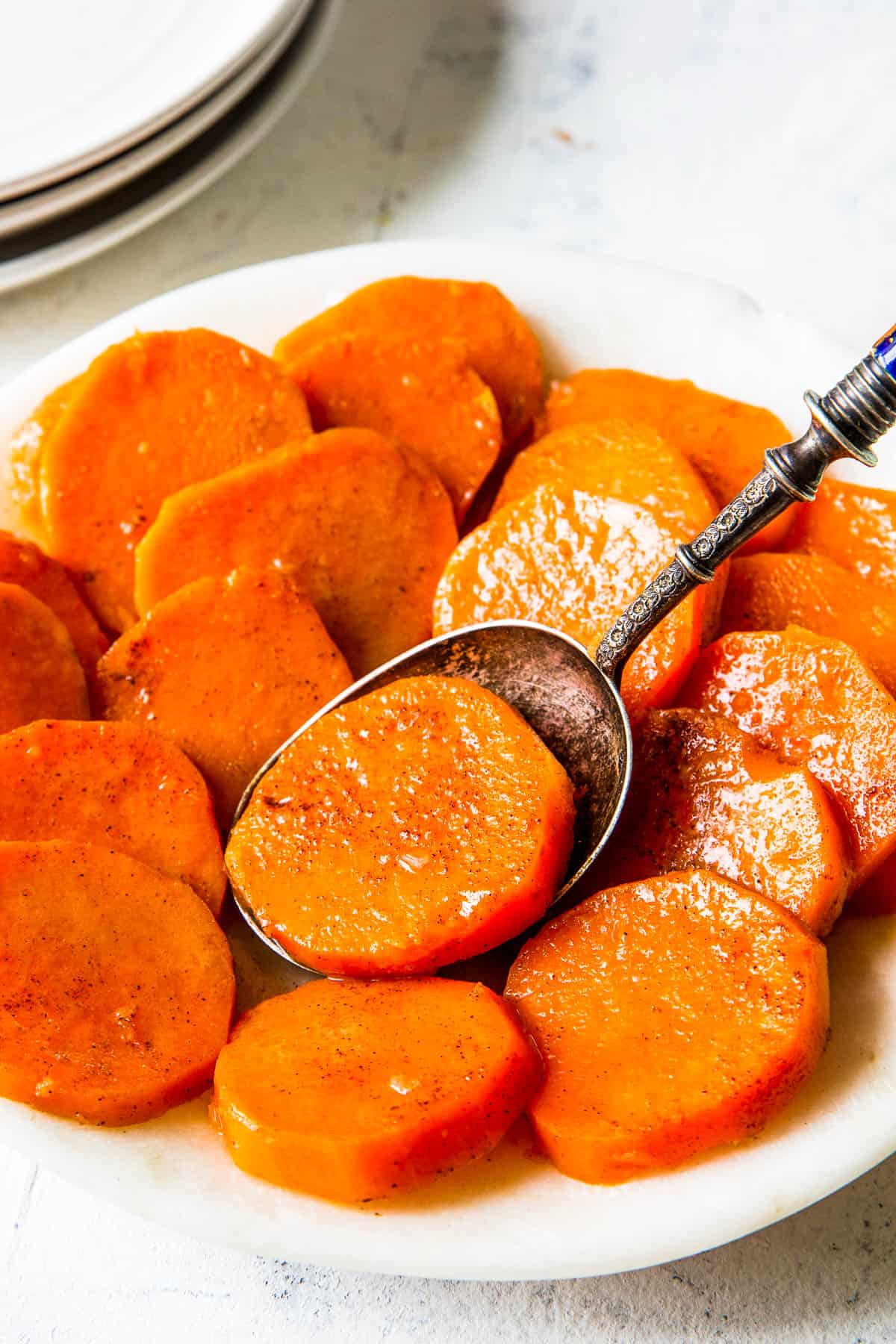 A white dish full of candied yams and a spoon.