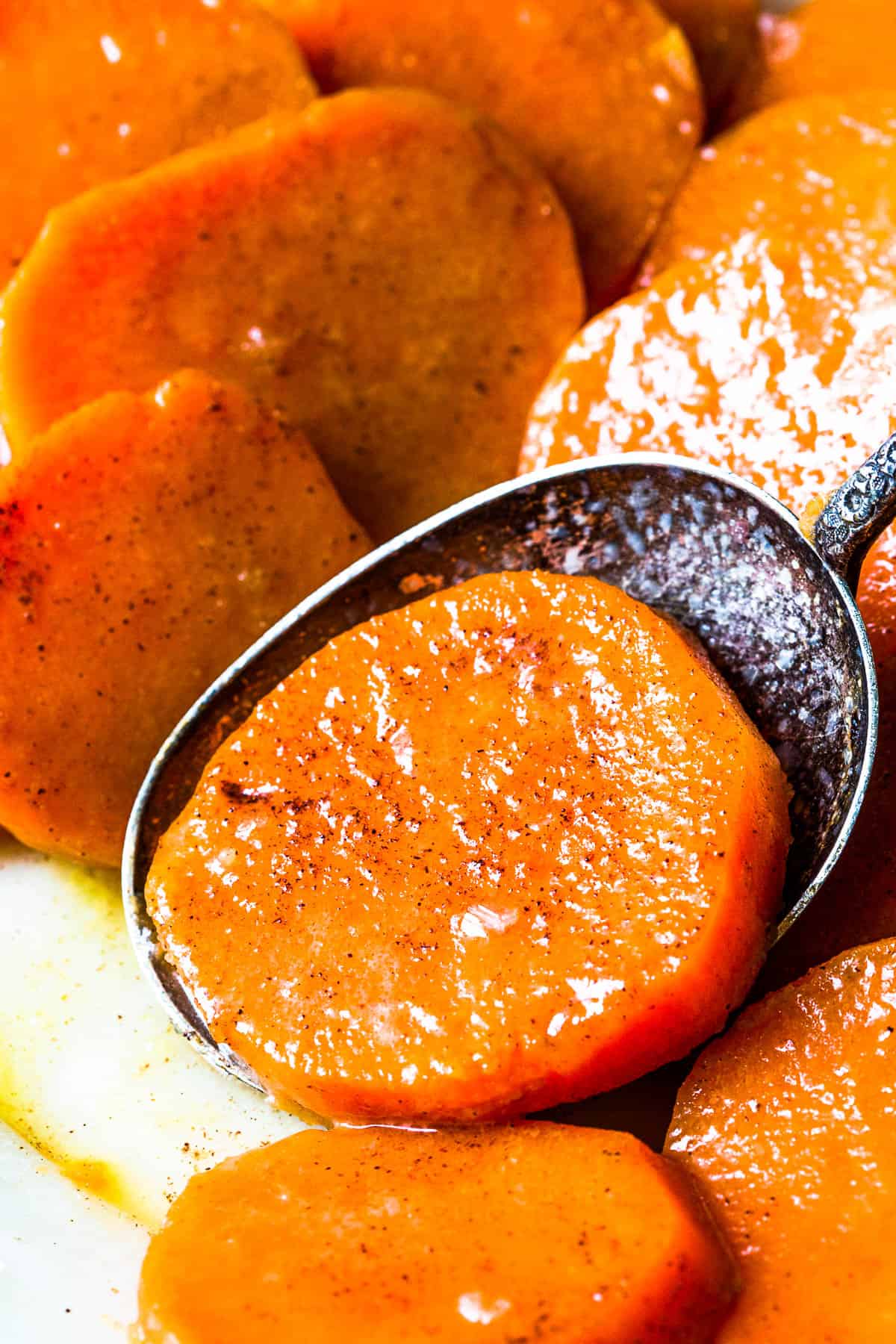 Candied yam slices with a serving spoon scooping up one of the slices.