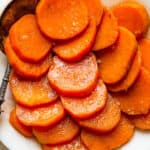 A white serving dish with sliced candied sweet potatoes and a serving spoon.