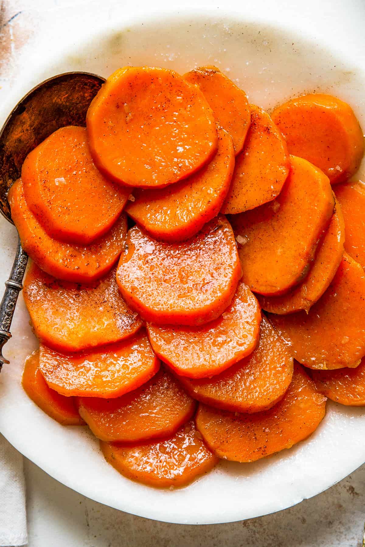 A white serving dish with sliced candied sweet potatoes and a serving spoon.