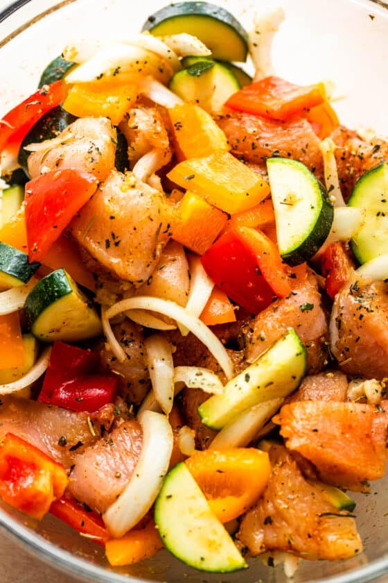 chicken pieces, sliced zucchini, peppers, and onions in a glass mixing bowl.