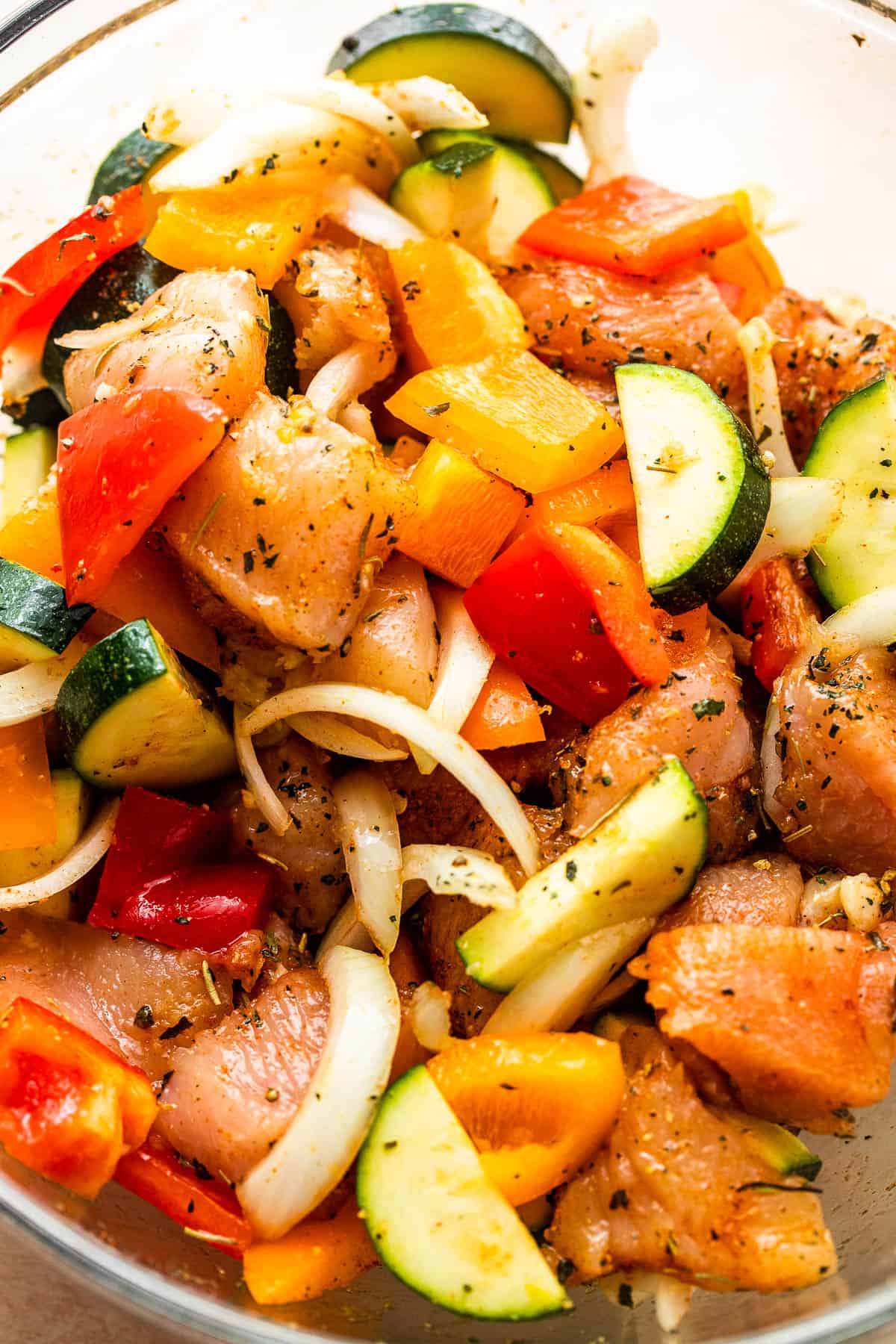 chicken pieces, sliced zucchini, peppers, and onions in a glass mixing bowl.